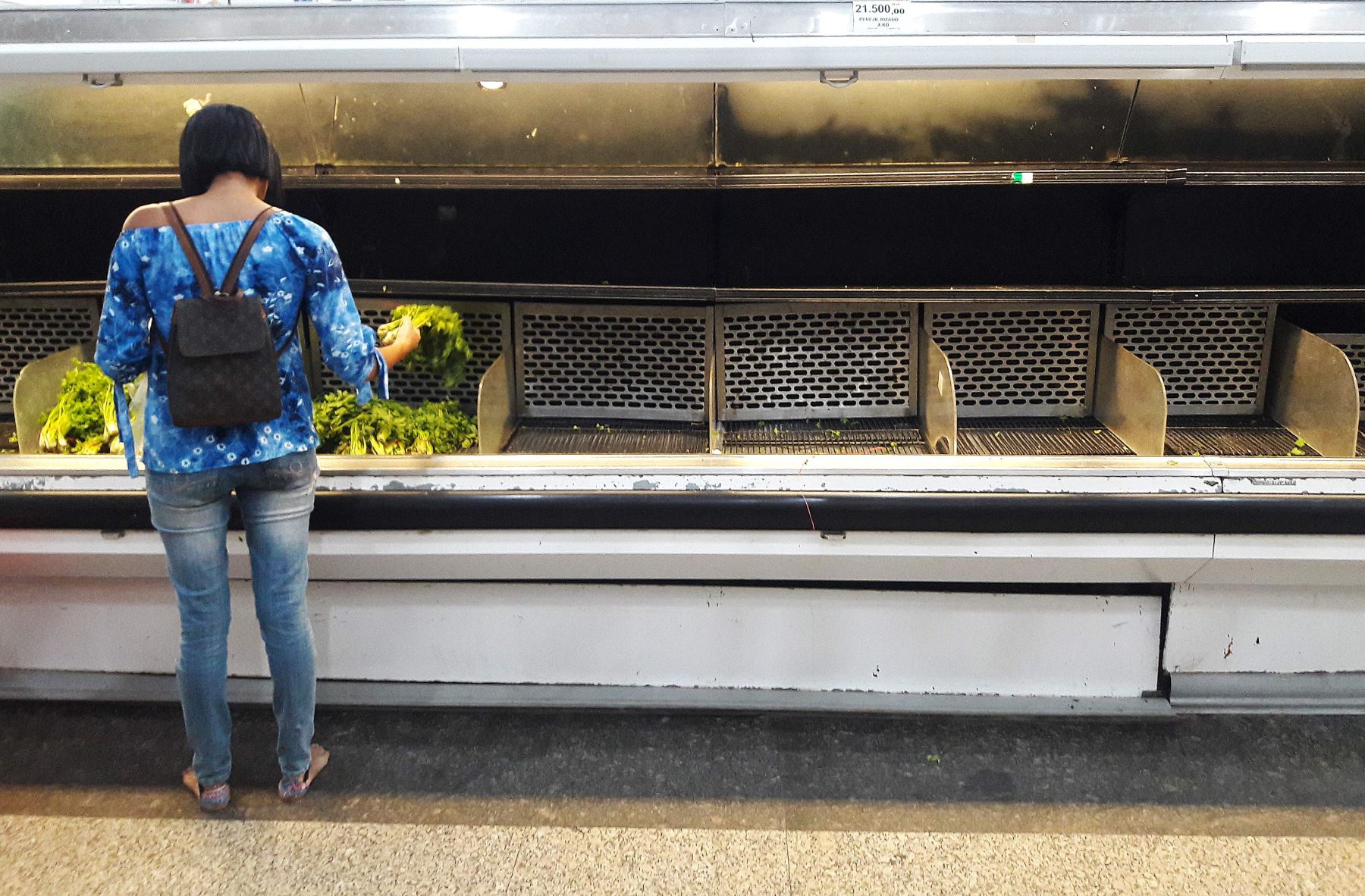 Mujer compra vegetales en vacío anaquel de Caracas. Foto: AFP