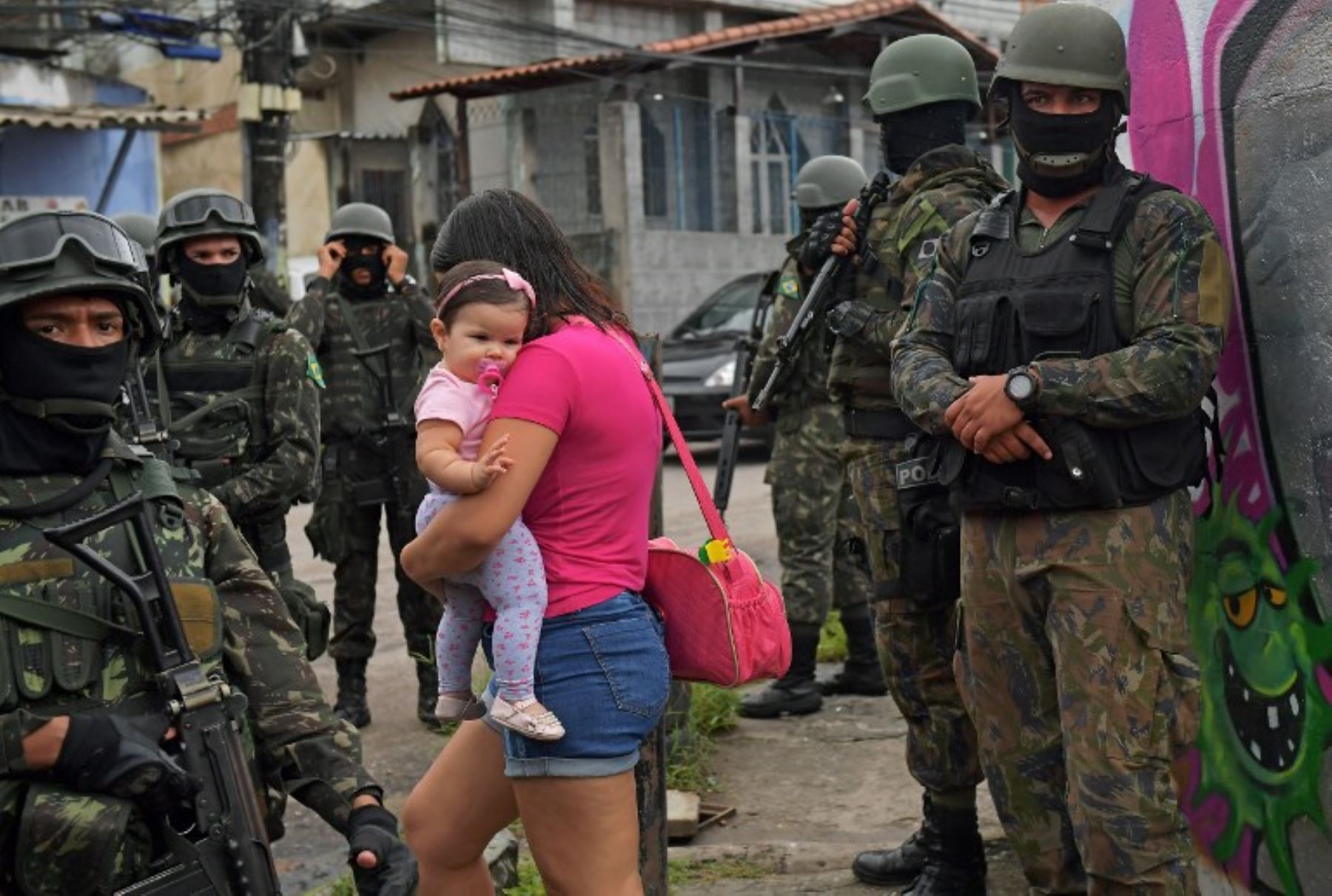 Una mujer carga a su hijo cuando pasa junto a la policía militar patrullando cerca de la favela de Vila Kennedy, en Río de Janeiro. Foto: AFP