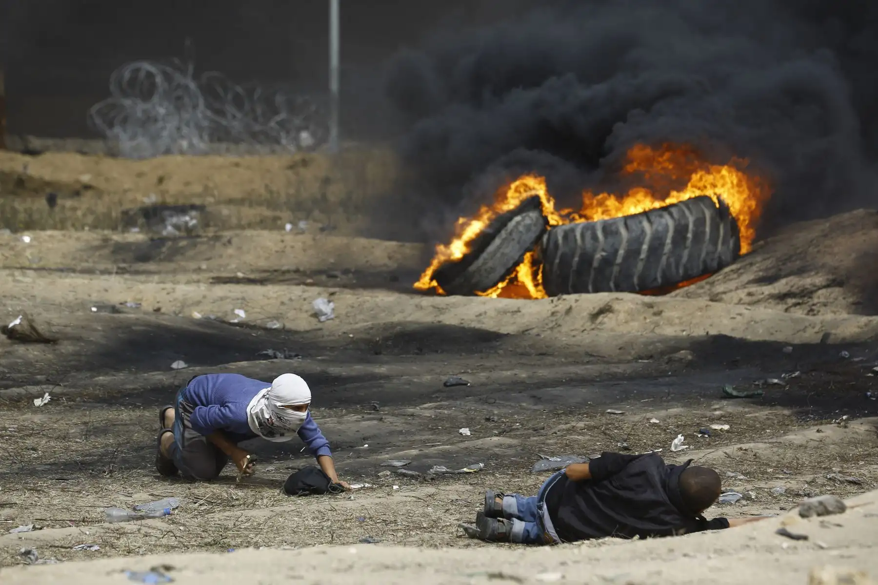Un manifestante palestino se arrastra para ayudar a un camarada a quemar neumáticos durante los enfrentamientos con las fuerzas israelíes al otro lado de la frontera en Gaza. AFP