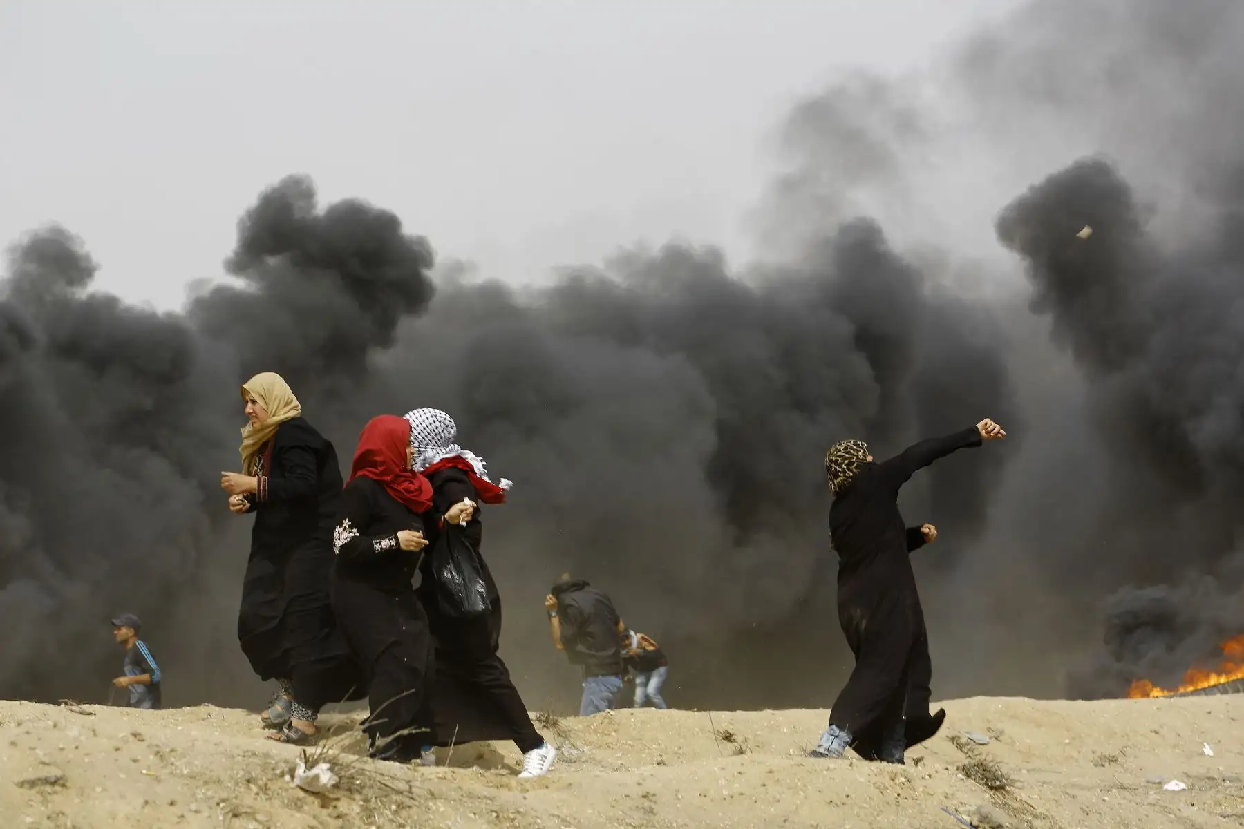 Las mujeres palestinas arrojan piedras más allá de la nube de humo al quemar neumáticos durante los enfrentamientos con las fuerzas israelíes en la Franja de Gaza. AFP