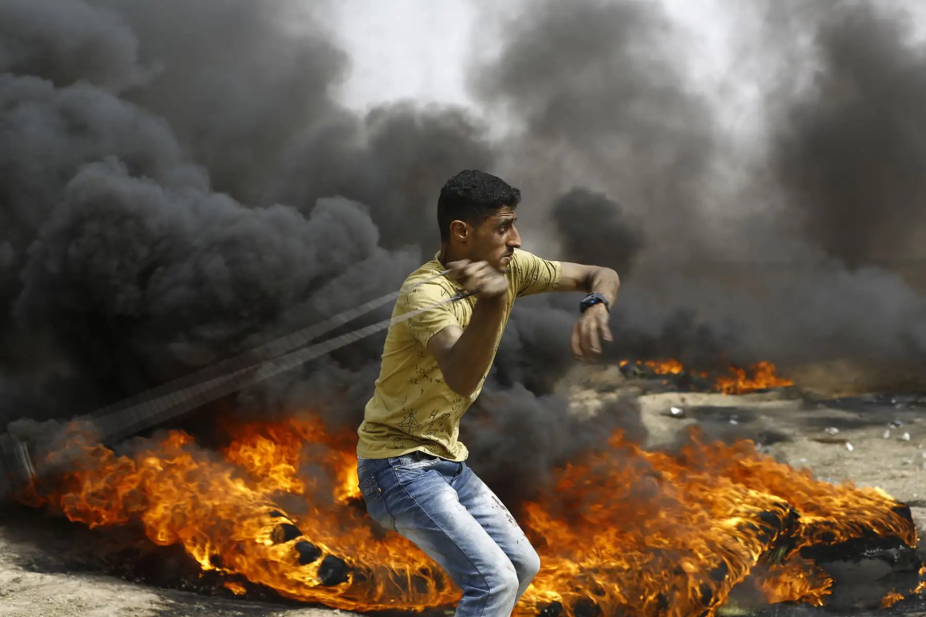 Un palestino lanza un tiro con onda mientras se queman  neumáticos durante los enfrentamientos con las fuerzas israelíes en Gaza. AFP