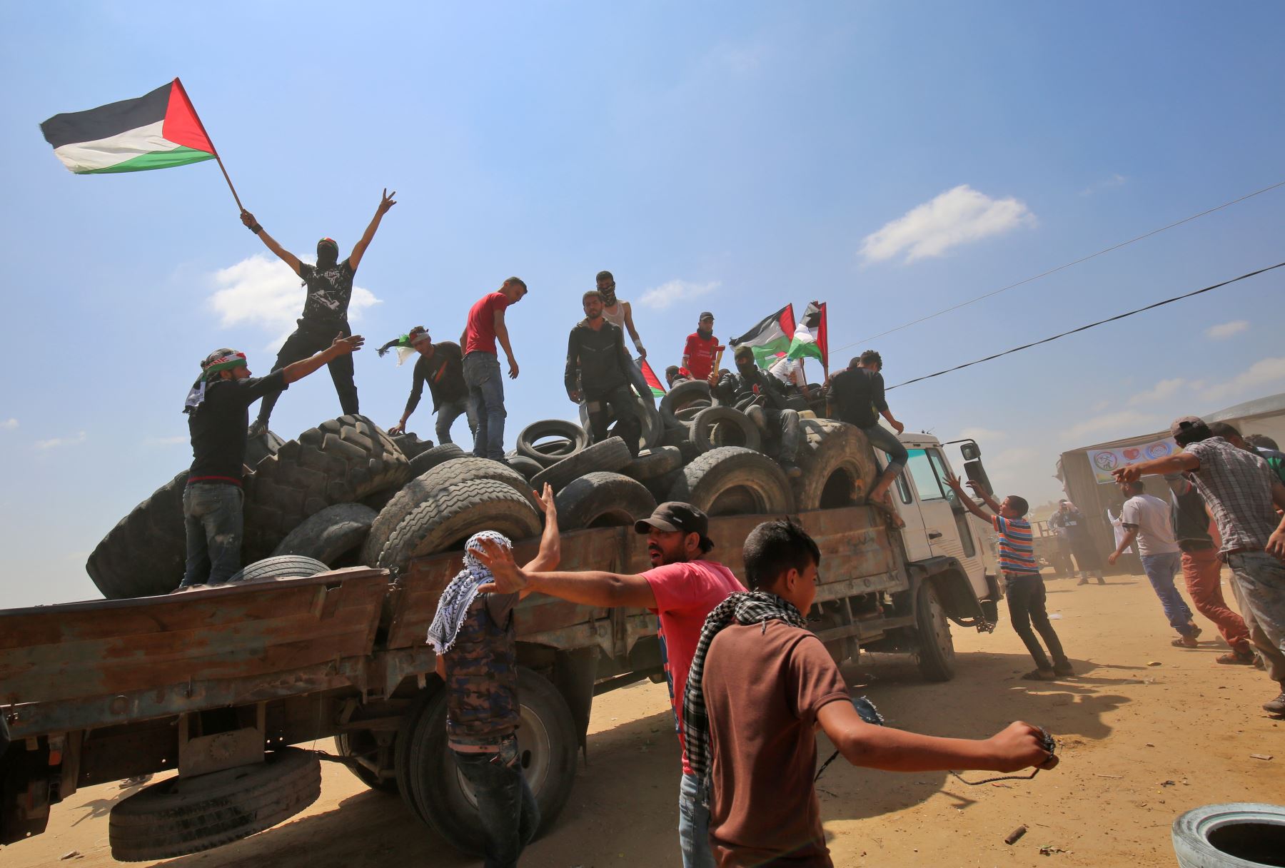 Un hombre enmascarado agita una bandera palestina mientras se para con otros en la parte trasera de un camión lleno de llantas que se quemaron durante las manifestaciones cerca de la frontera con Israel, al este de Khan Yunis en el sur de la Franja de Gaza. AFP