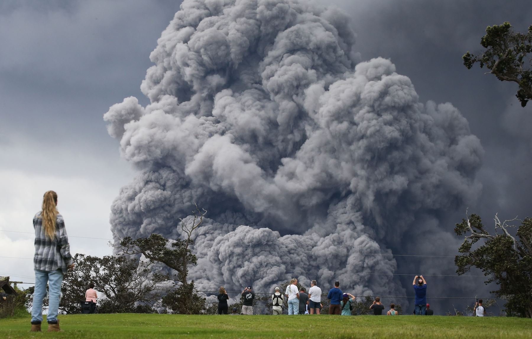 La gente mira en un campo de golf cuando una pluma de ceniza se eleva a lo lejos del volcán Kilauea, en Hawái. Foto: AFP.