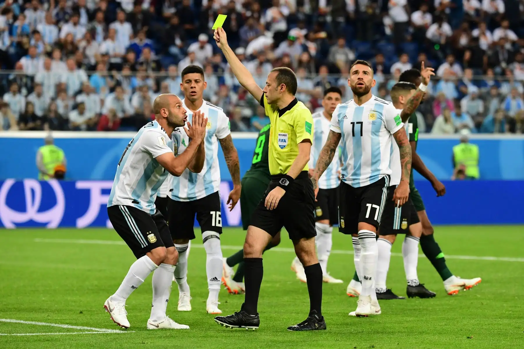 El árbitro turco Cuneyt Cakir (C) presenta al centrocampista argentino Javier Mascherano (L) con una tarjeta amarilla durante el partido de fútbol del Grupo D de la Copa Mundial Rusia 2018 entre Nigeria y Argentina en el Estadio de San Petersburgo el 26 de junio de 2018. / AFP
