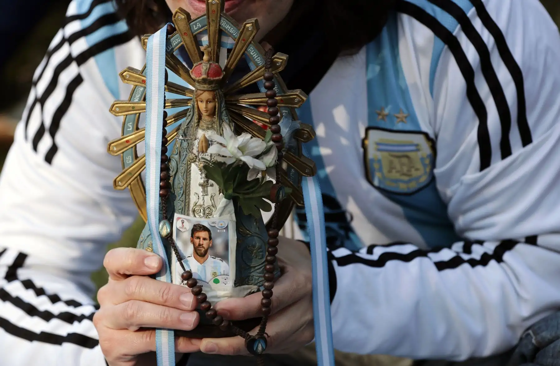 Una fan de Argentina sostiene una imagen de la Virgen del Luján con una foto de Lionel Messi, mientras observa el partido de la Copa Mundial FIFA de Rusia 2018 entre Argentina e Islandia en una pantalla grande en la plaza San Martín en Buenos Aires, el 16 de junio del 2018. Foto: AFP.