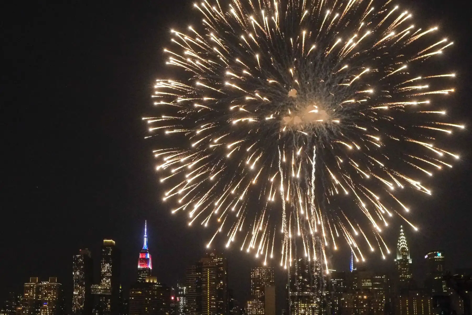 El Empire State Building se ilumina en azul, blanco y rojo mientras la gente mira los fuegos artificiales del 4 de julio de Macy