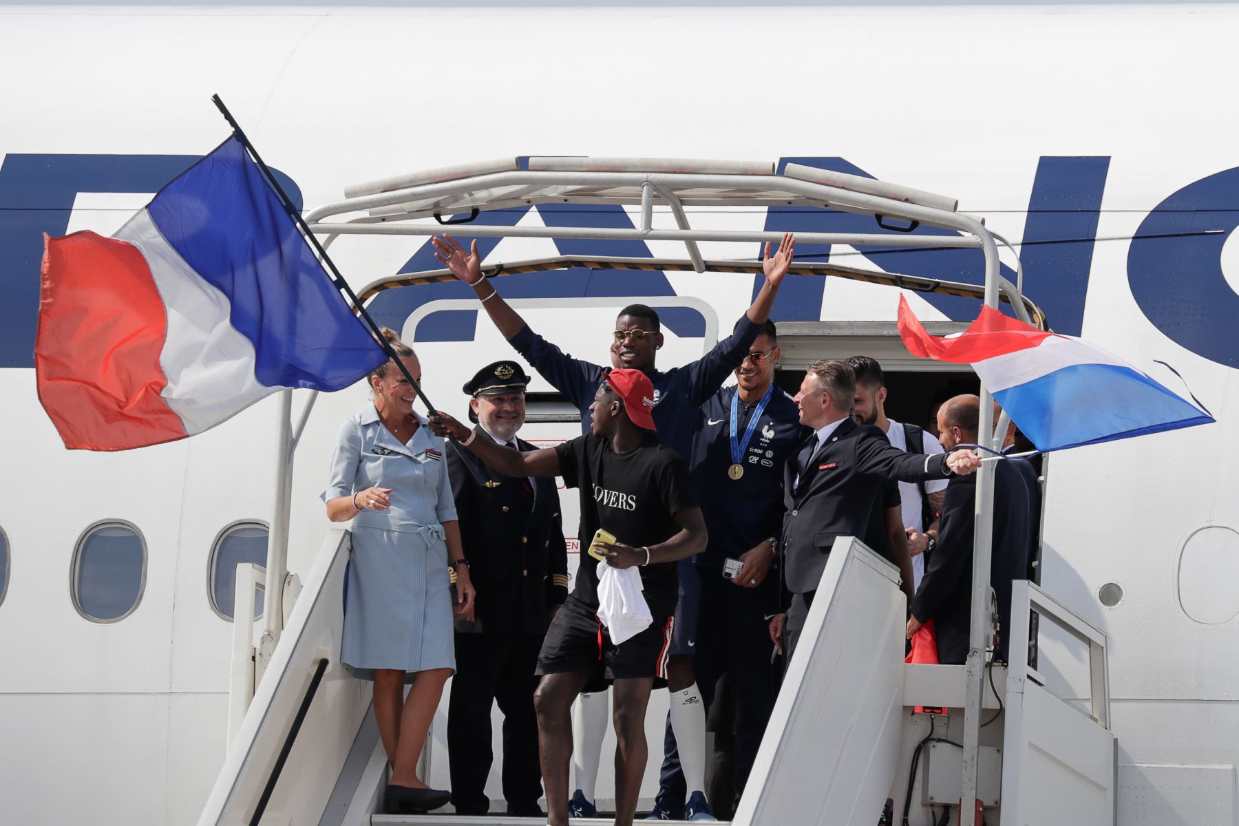 El defensor de Francia Benjamin Mendy  agita la bandera nacional francesa junto al centrocampista francés Paul Pogba  mientras desembarcan del avión a su llegada al aeropuerto Roissy-Charles de Gaulle en las afueras de París, después ganando el partido de fútbol final de la Copa Mundial Rusia 2018. AFP