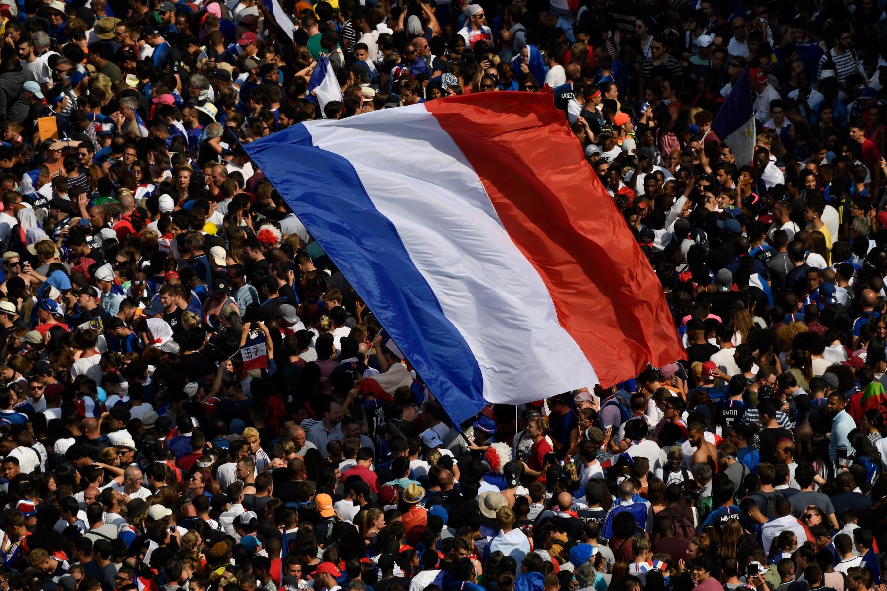 Los fanáticos agitan una gigantesca bandera nacional francesa mientras se reúnen en la avenida de los Campos Elíseos cerca del Arco del Triunfo en París, esperando   la llegada del equipo nacional de fútbol francés para las celebraciones por la victoria de la Copa del Mundo Rusia 2018. AFP