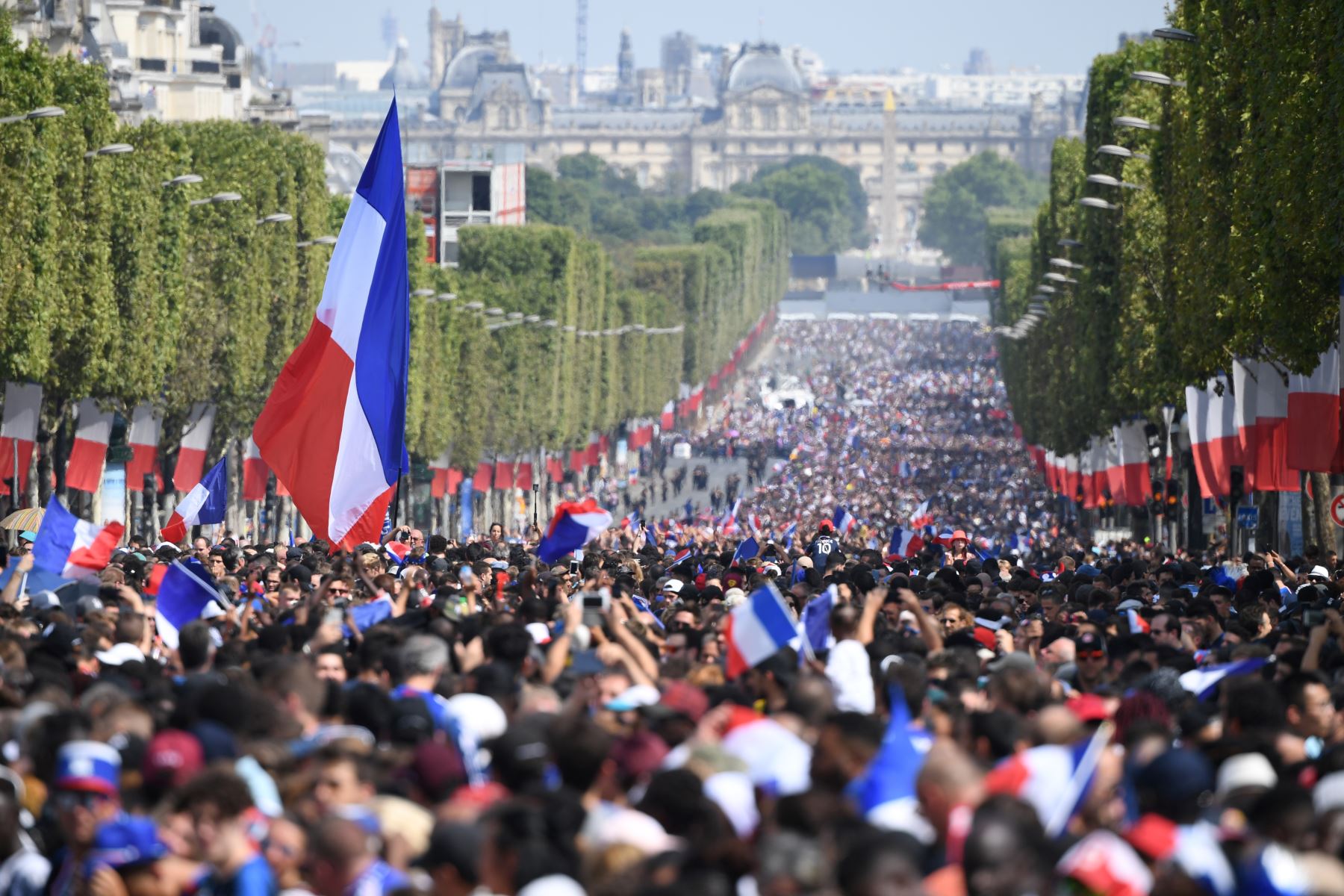 Los simpatizantes ondean banderas nacionales francesas mientras se reúnen en la avenida de los Campos Elíseos en París mientras esperan la llegada del equipo de fútbol nacional francés para las celebraciones después de que Francia ganó el partido de fútbol final de la Copa Mundial Rusia 2018 en la noche anterior. AFP