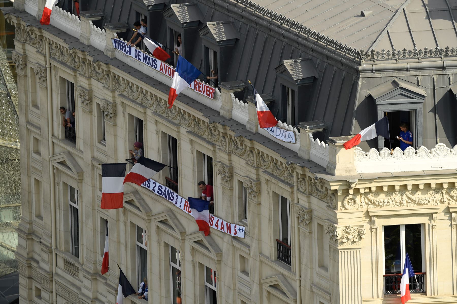 La gente agita banderas nacionales francesas desde las ventanas junto a pancartas que dicen "Gracias por hacernos soñar" y "Nunca dos sin tres, cita en cuatro años" en la avenida de los Campos Elíseos en París  como partidarios aguardan la llegada del equipo de fútbol nacional francés para las celebraciones por haber ganado la Copa Mundial de Rusia 2018. AFP