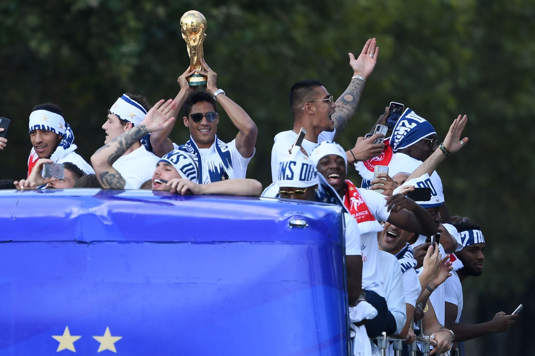 El defensor de Francia Raphael Varane sostiene el trofeo mientras celebra con sus compañeros de equipo en el techo de un autobús mientras desfila por la avenida Champs-Elysee en París. AFP
