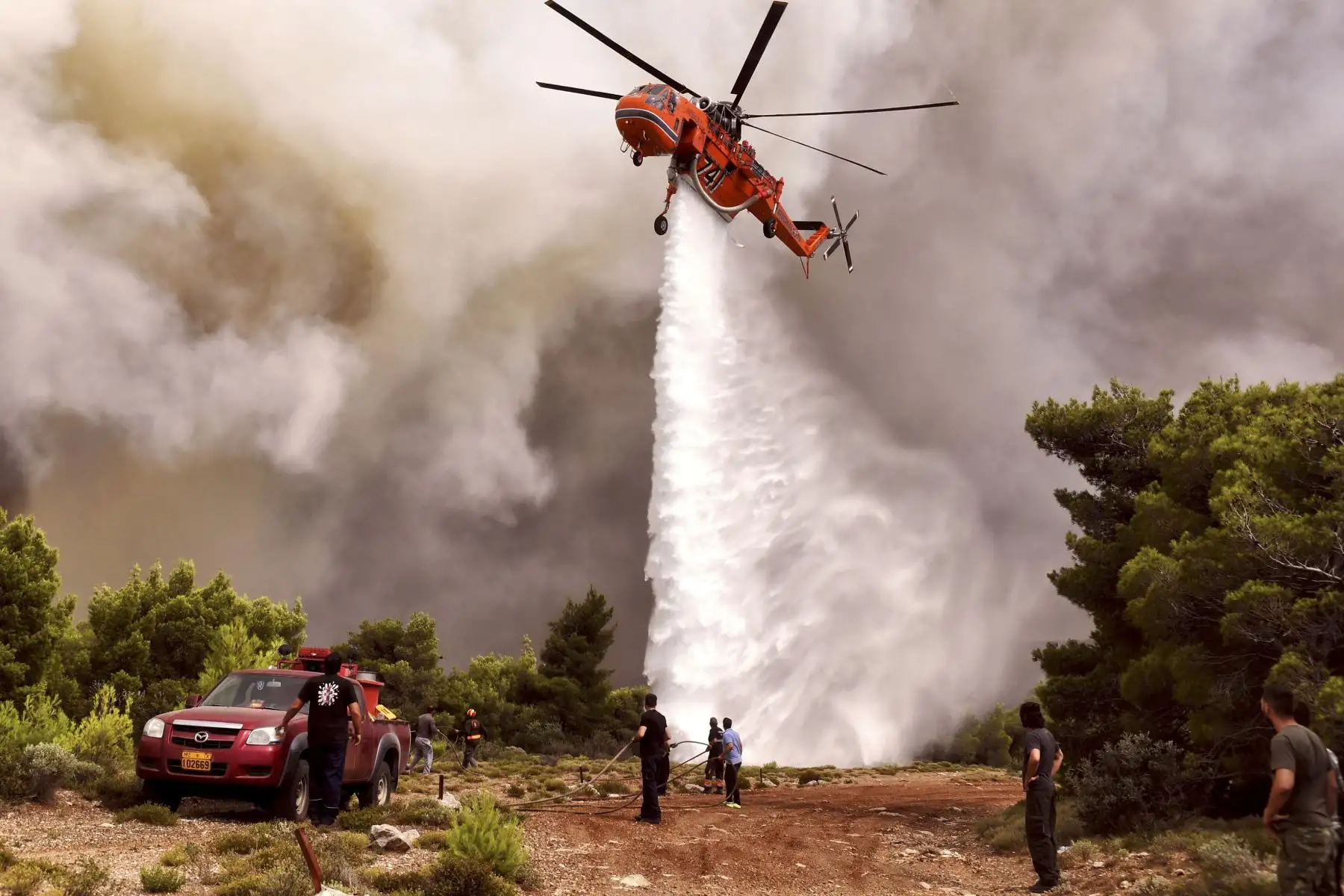 Un helicóptero de lucha contra incendios arroja agua para extinguir las llamas durante un incendio forestal en la aldea de Kineta, cerca de Atenas, el 24 de julio de 2018. AFP