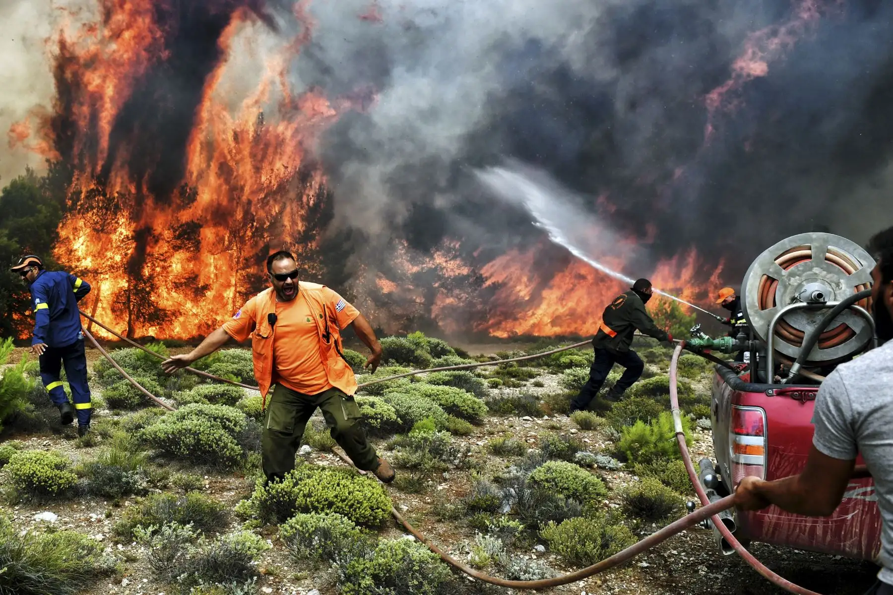 Los bomberos y voluntarios intentan extinguir las llamas durante un incendio forestal en la aldea de Kineta, cerca de Atenas. AFP