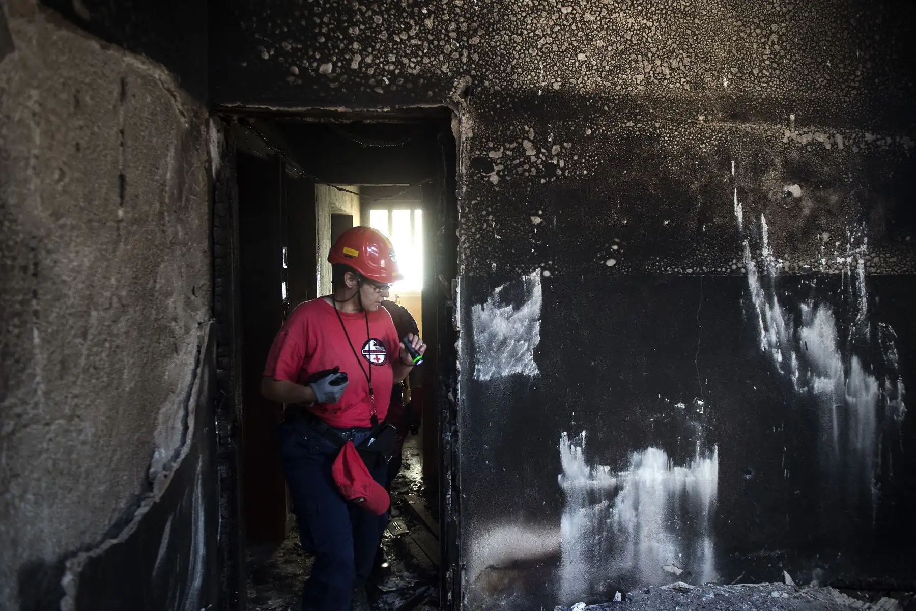 Una foto tomada el 25 de julio de 2018 muestra autos quemados tras un incendio forestal en el via. Un miembro de un equipo de rescate busca personas desaparecidas dentro de una casa quemada en el pueblo de Mati, cerca de Atenas. AFP
