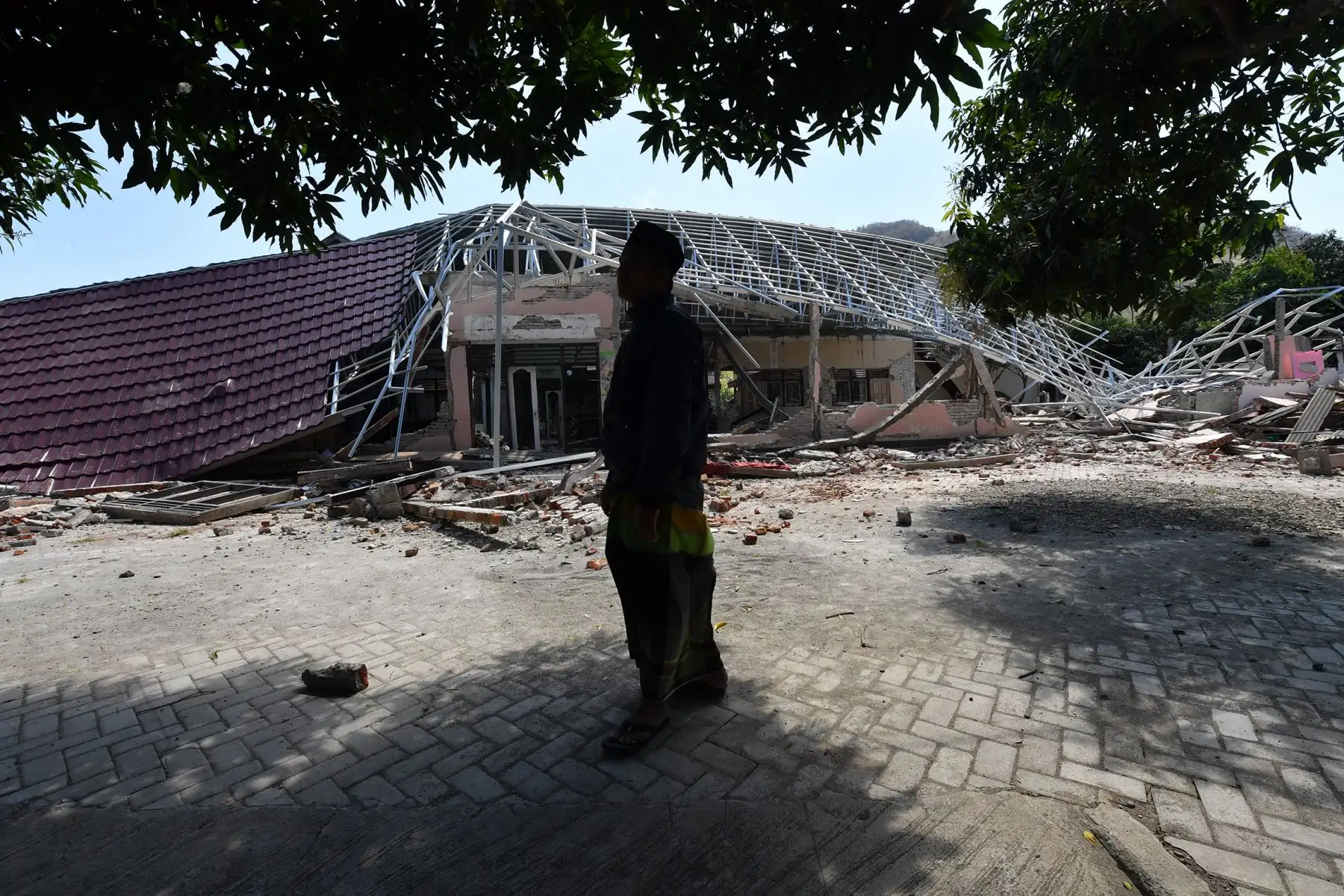 Un clérigo musulmán se para frente a una escuela religiosa destruida en Bangsal, en la isla indonesia de Lombok, el 6 de agosto de 2018, un día después de que un terremoto de 6.9 grados de magnitud sacudiera la zona. AFP