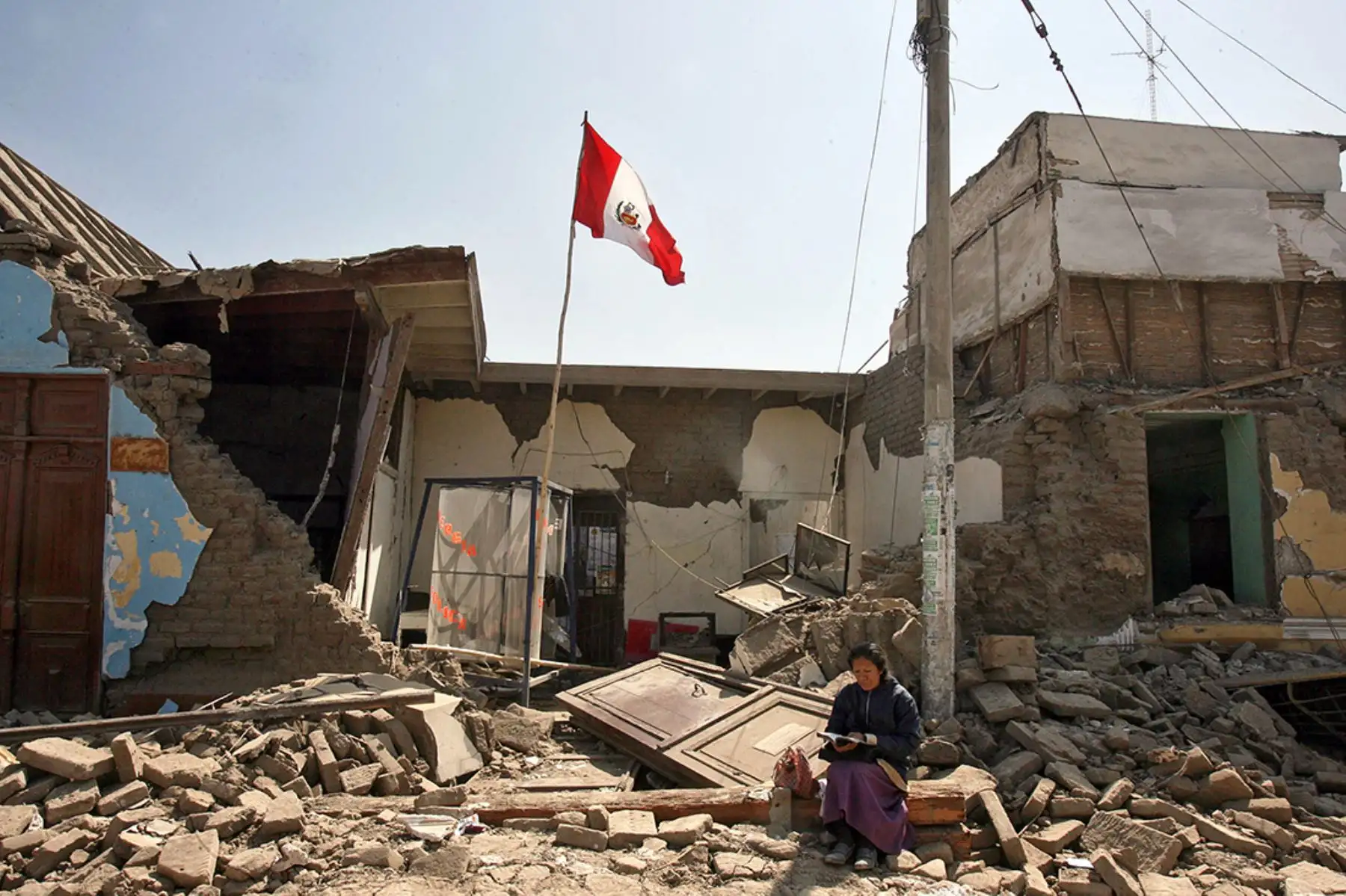 Una mujer lee la Biblia frente a su casa destruida (16 agosto 2007). Foto: AFP