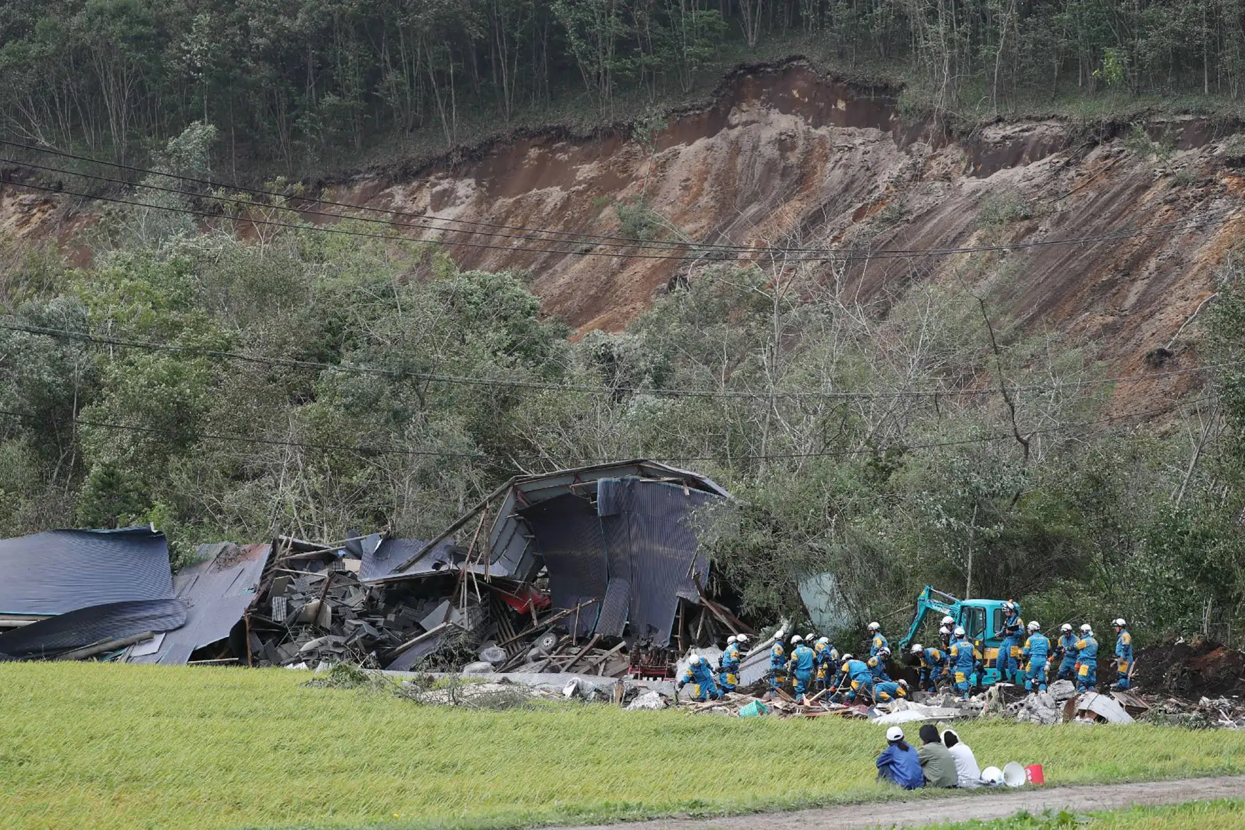 Los residentes locales observan cómo los equipos de rescate buscan personas desaparecidas en un área afectada por los deslizamientos de tierra provocados por un terremoto en la ciudad de Atsuma, prefectura de Hokkaido, el 7 de septiembre de 2018.
Los trabajadores de rescate japoneses con excavadoras y perros rastreadores buscaron en el barro el 6 de septiembre para encontrar sobrevivientes de un deslizamiento de tierra que enterró casas después de un poderoso terremoto, ya que el número de muertos aumentó