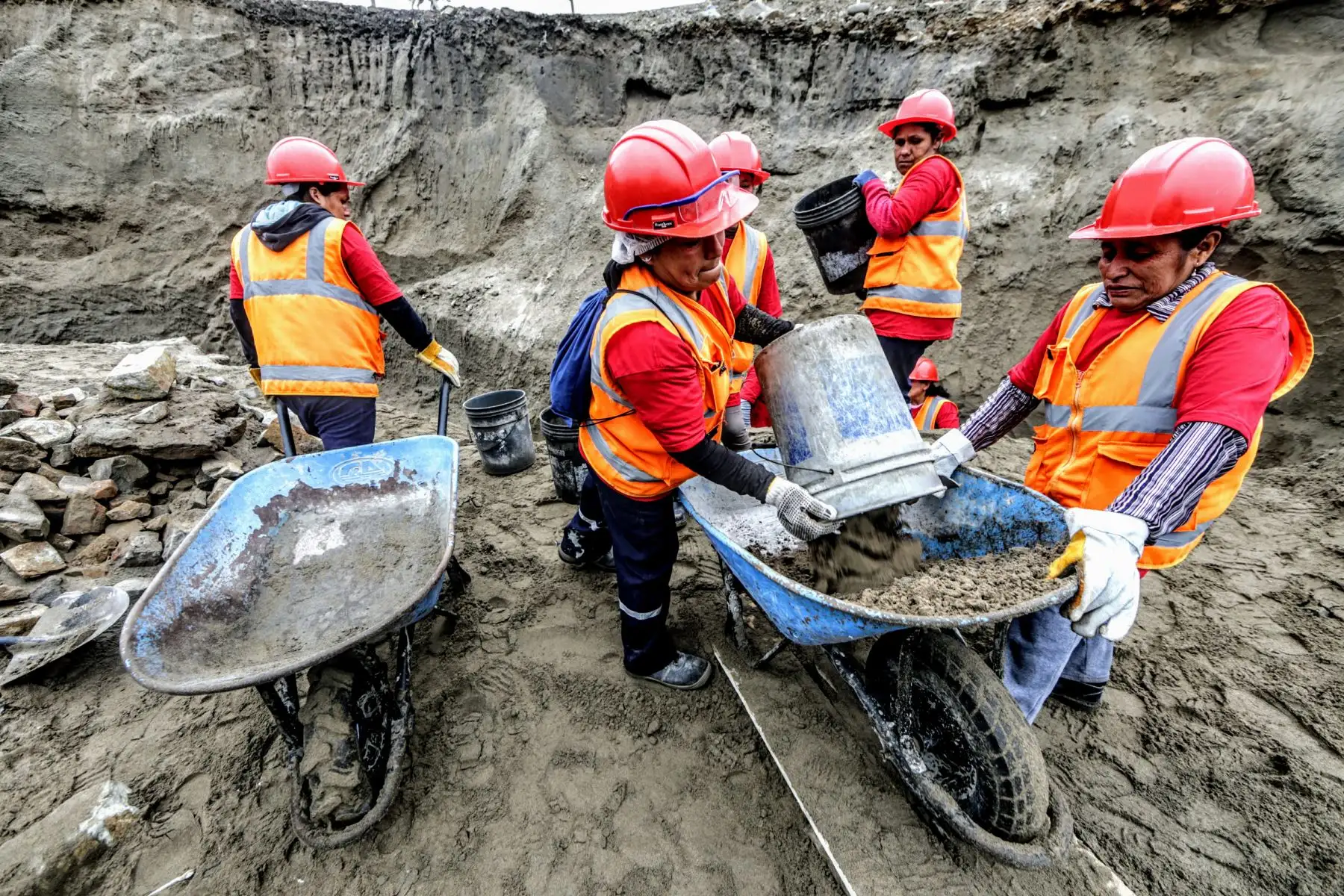 Las operarias llenan con una manguera un bidón de agua. Ayudan a sus compañeras a elaborar la mezcla de cemento, que, a su vez, servirá para el asentado de piedra y el solaqueo del muro de contención.  Foto: ANDINA/Luis Iparraguirre