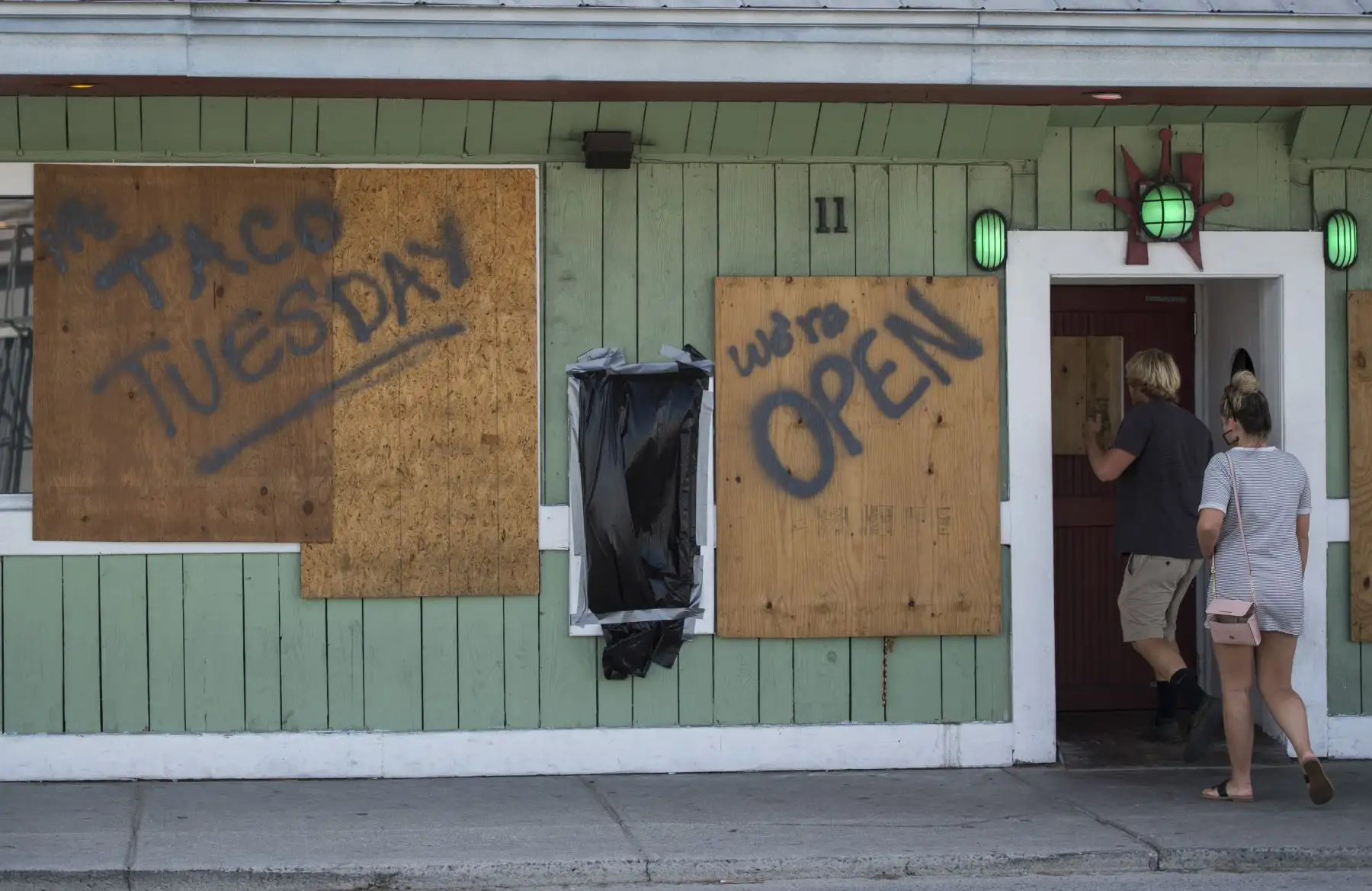 Dos personas ingresan a un restaurante con ventanas entabladas para perpetrar la llegada del huracán Florence a la playa Wrightsville, Carolina del Norte, el 11 de septiembre de 2018. /AFP