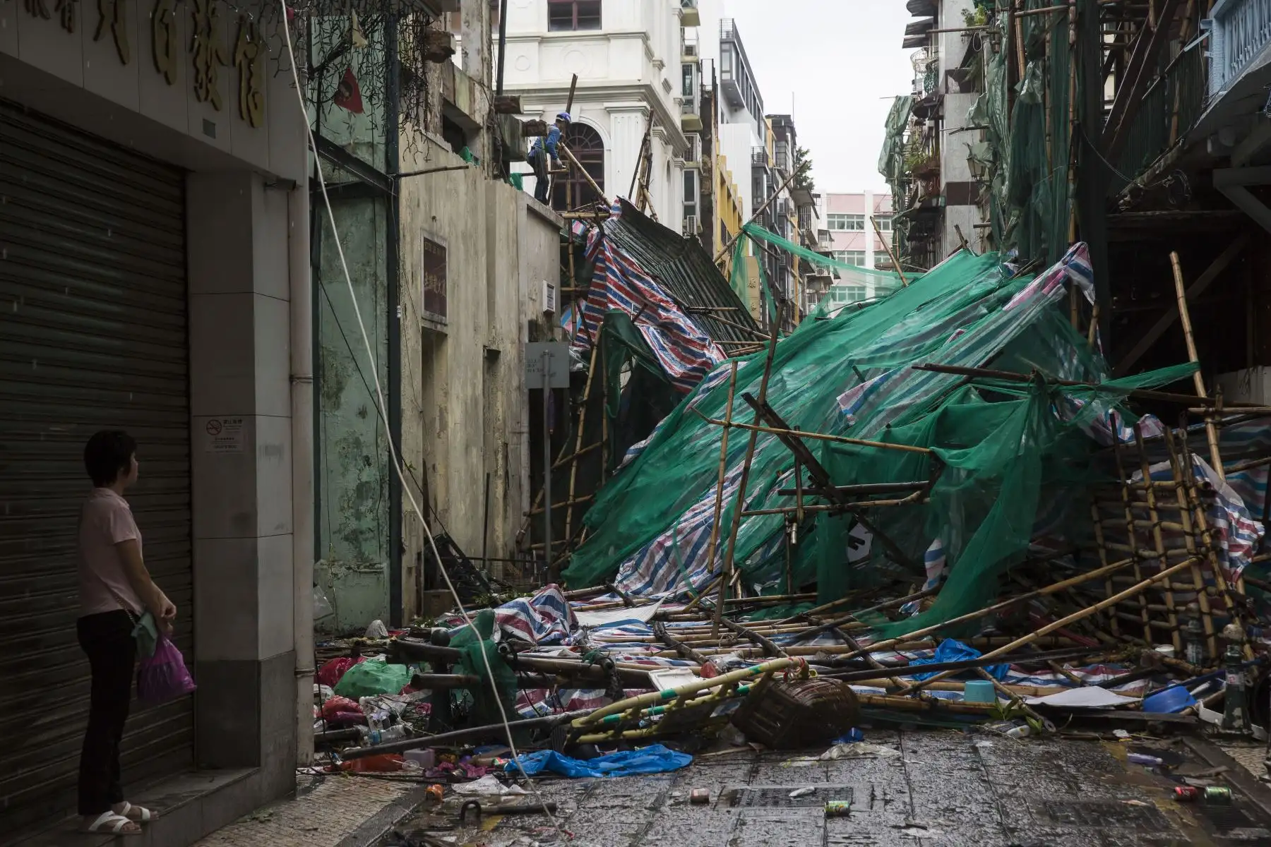 Una mujer se ve como una trabajadora (parte superior L) quita los andamios derribados por los fuertes vientos, un día después de que el tifón Mangkhut azotara Macao el 17 de septiembre de 2018.  AFP