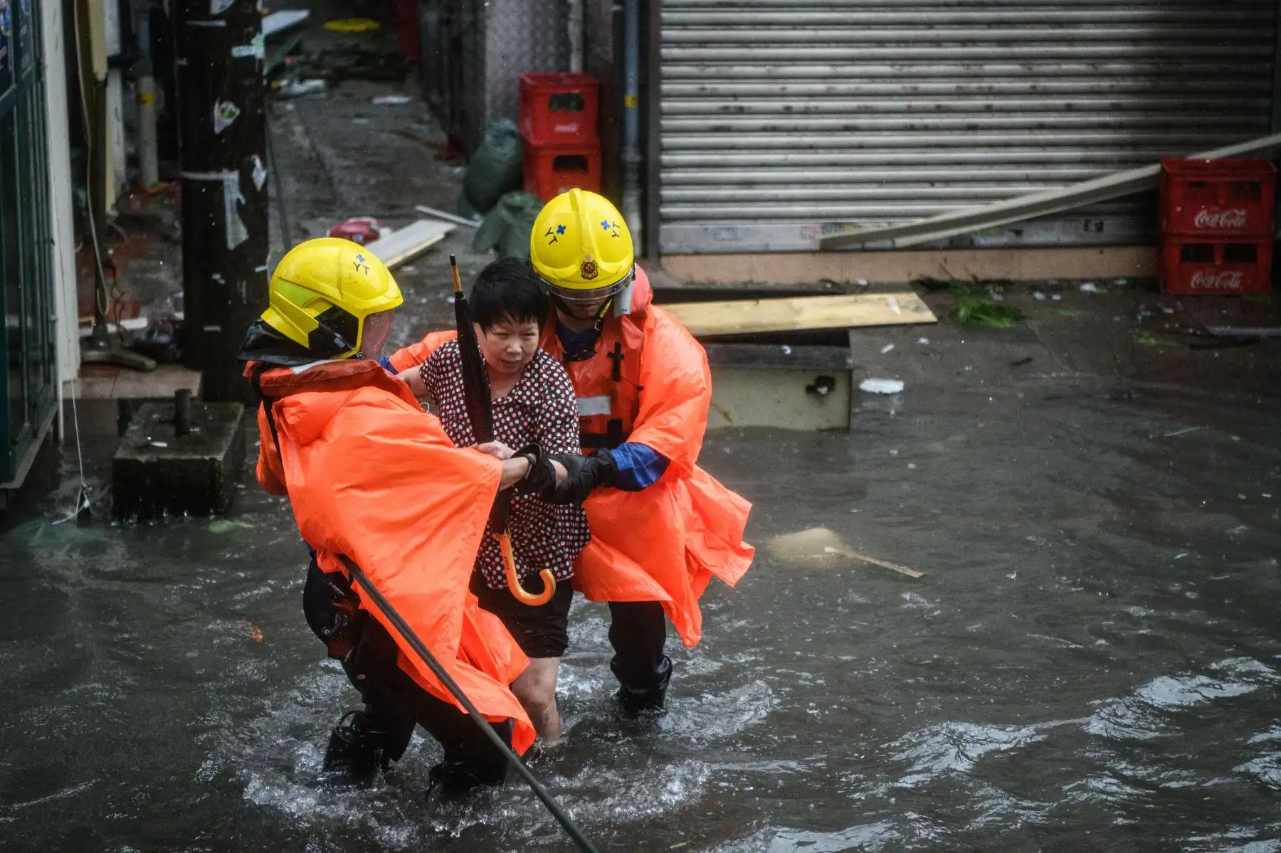 Los miembros de rescate de incendios ayudan a una mujer a cruzar una calle inundada en el pueblo de Lei Yu Mun durante el Súper Tifón Mangkhut en Hong Kong. AFP