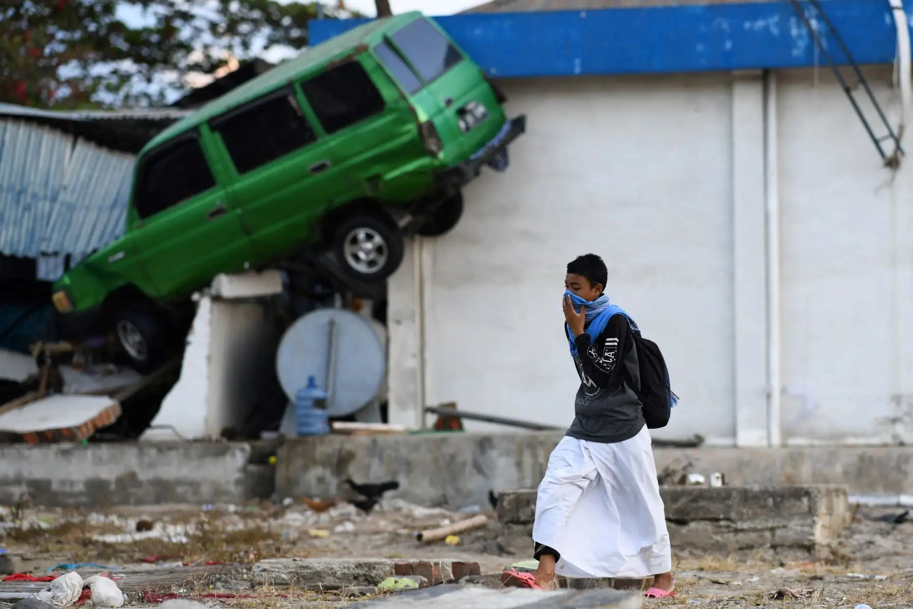 Un sobreviviente camina bajo un automóvil chocado contra un edificio en Palu, Sulawesi Central, Indonesia, el 1 de octubre de 2018, luego de que un terremoto y un tsunami azotaran la zona. AFP