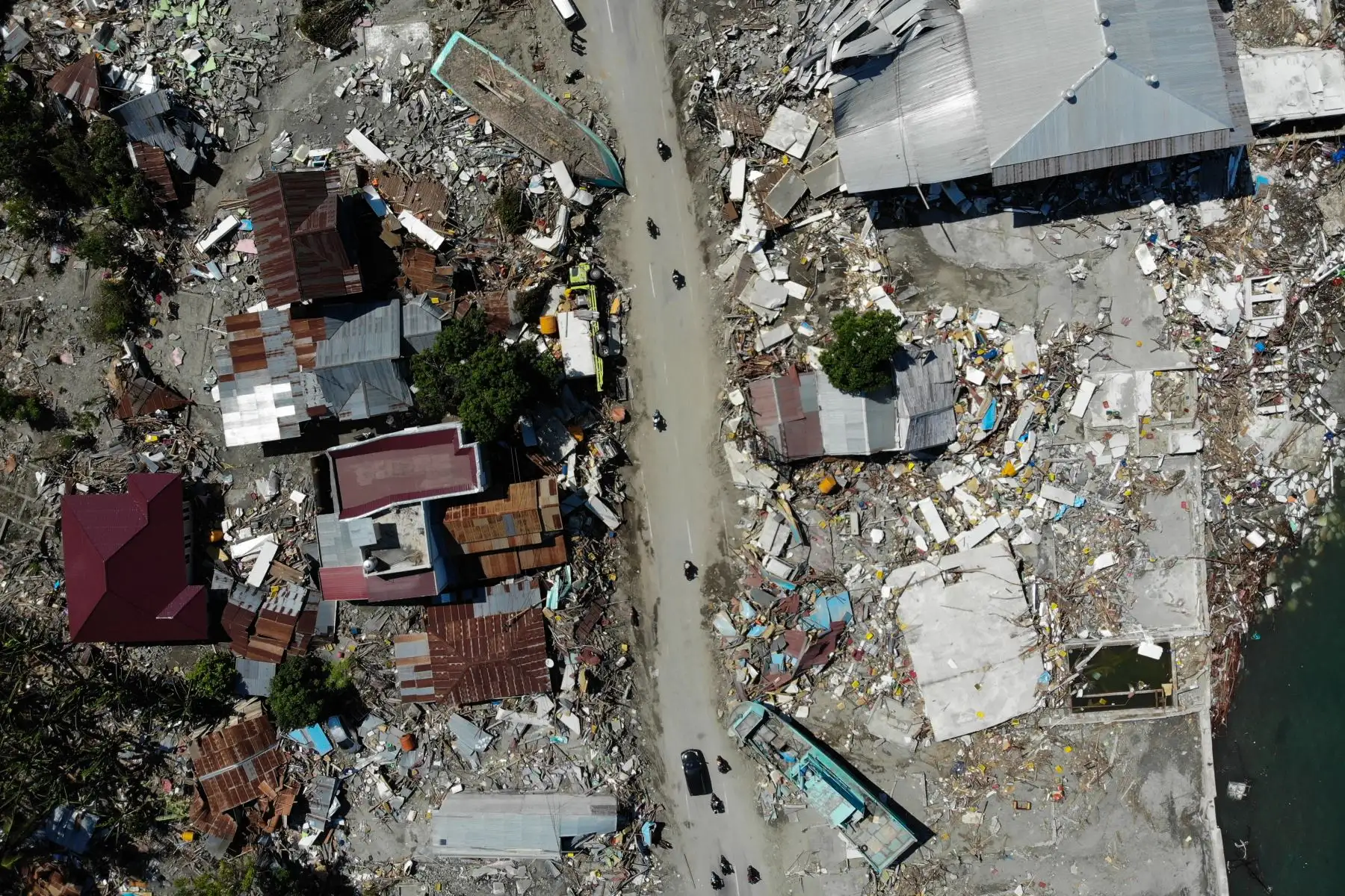 Esta foto aérea muestra personas (C) conduciendo más allá de un bote lavado y edificios derrumbados en Palu el 1 de octubre de 2018, después de que un terremoto y un tsunami golpearon la zona. AFP
