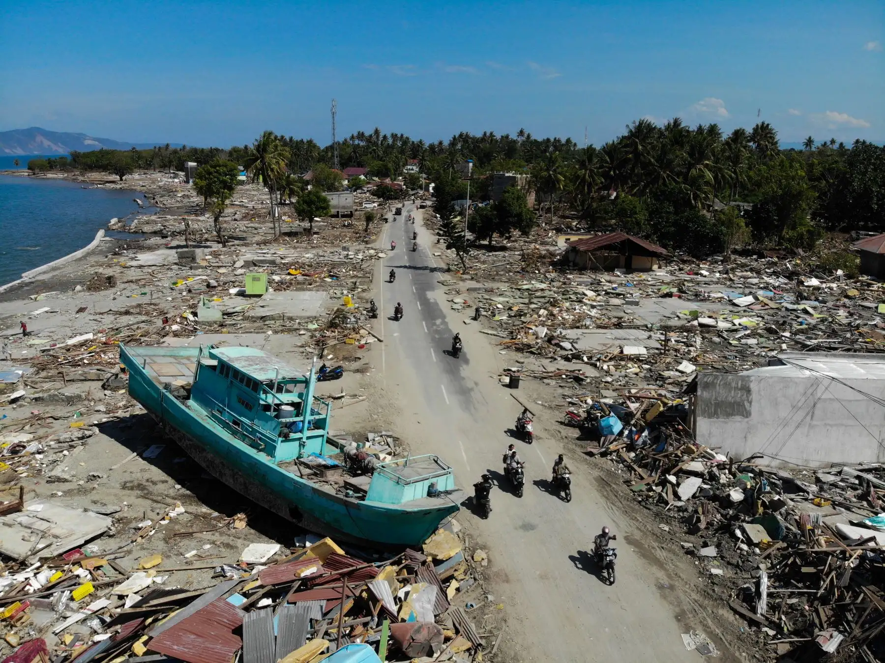 La gente pasa frente a un bote lavado y edificios derrumbados en Palu el 1 de octubre de 2018, después de que un terremoto y un tsunami azotaran la zona. AFP