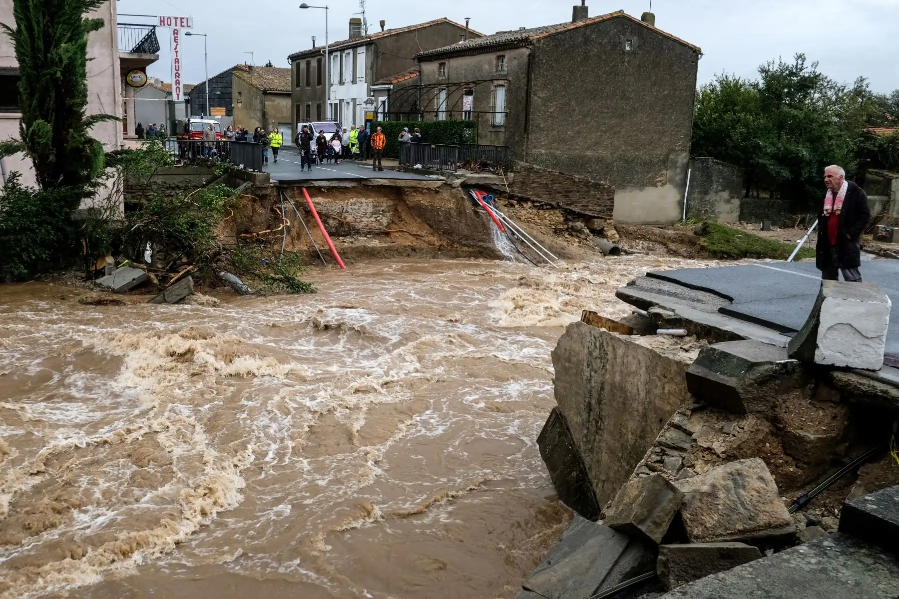 Las personas se paran en la carretera junto a un puente sobre el río Trapel que se derrumbó en el departamento de Aude después de haber sido gravemente afectada por fuertes tormentas de lluvia que inundaron partes del suroeste de Francia.  AFP