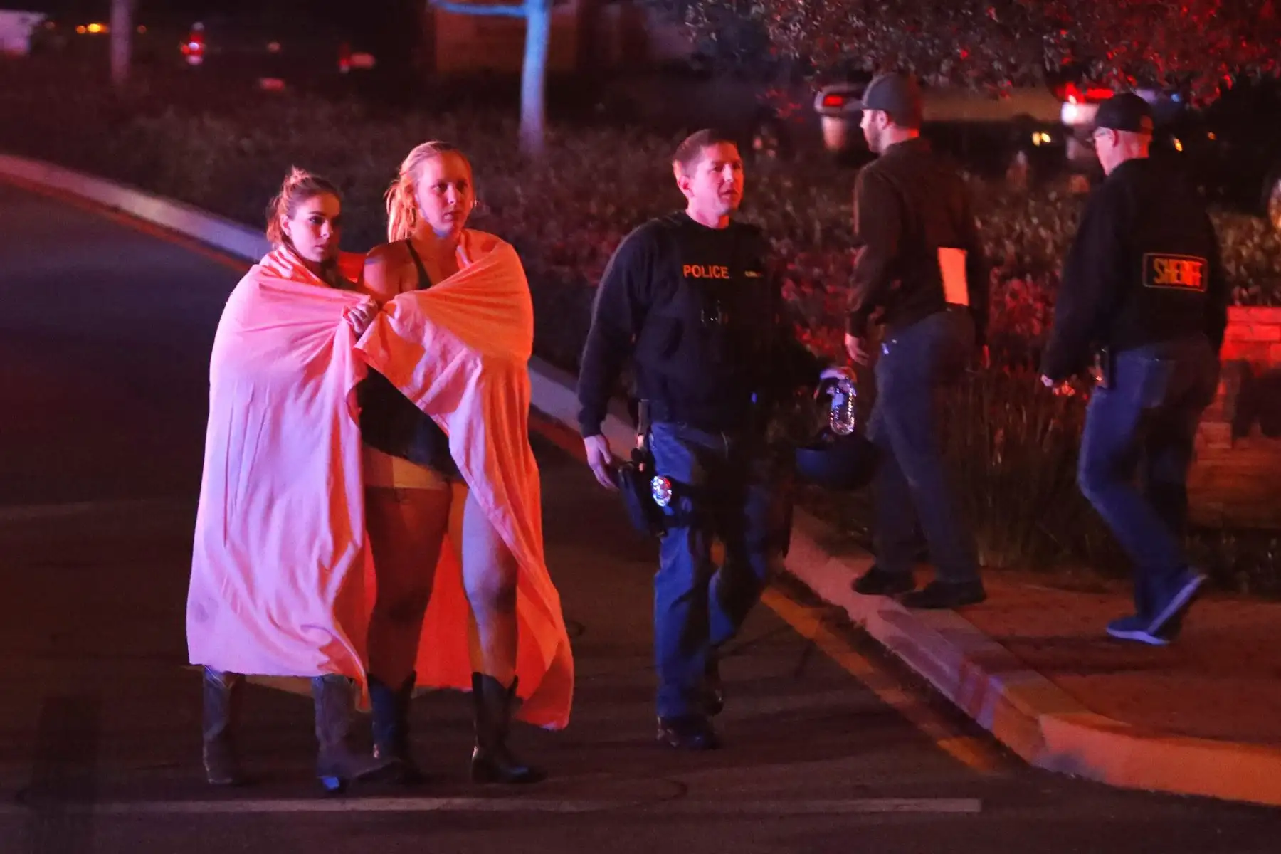 Dos mujeres envueltas en una s · bana abandonan el · rea del tiroteo cerca del bar Borderline en la localidad de Thousand Oaks, California, Estados Unidos, hoy 8 de noviembre de 2018 Al menos 12 personas han muerto en este tiroteo perpetrado por un individuo sin identificar, que también ha sido encontrado muerto en el interior del bar. EFE