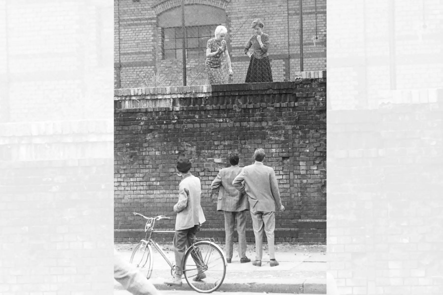 Una imagen  tomada el 26 de agosto de 1961 muestra a dos hombres en el lado oeste del muro de Berlín conversando con sus amigas detrás de una cerca en la estación de tren Stettiner Bahnhof. Foto: AFP