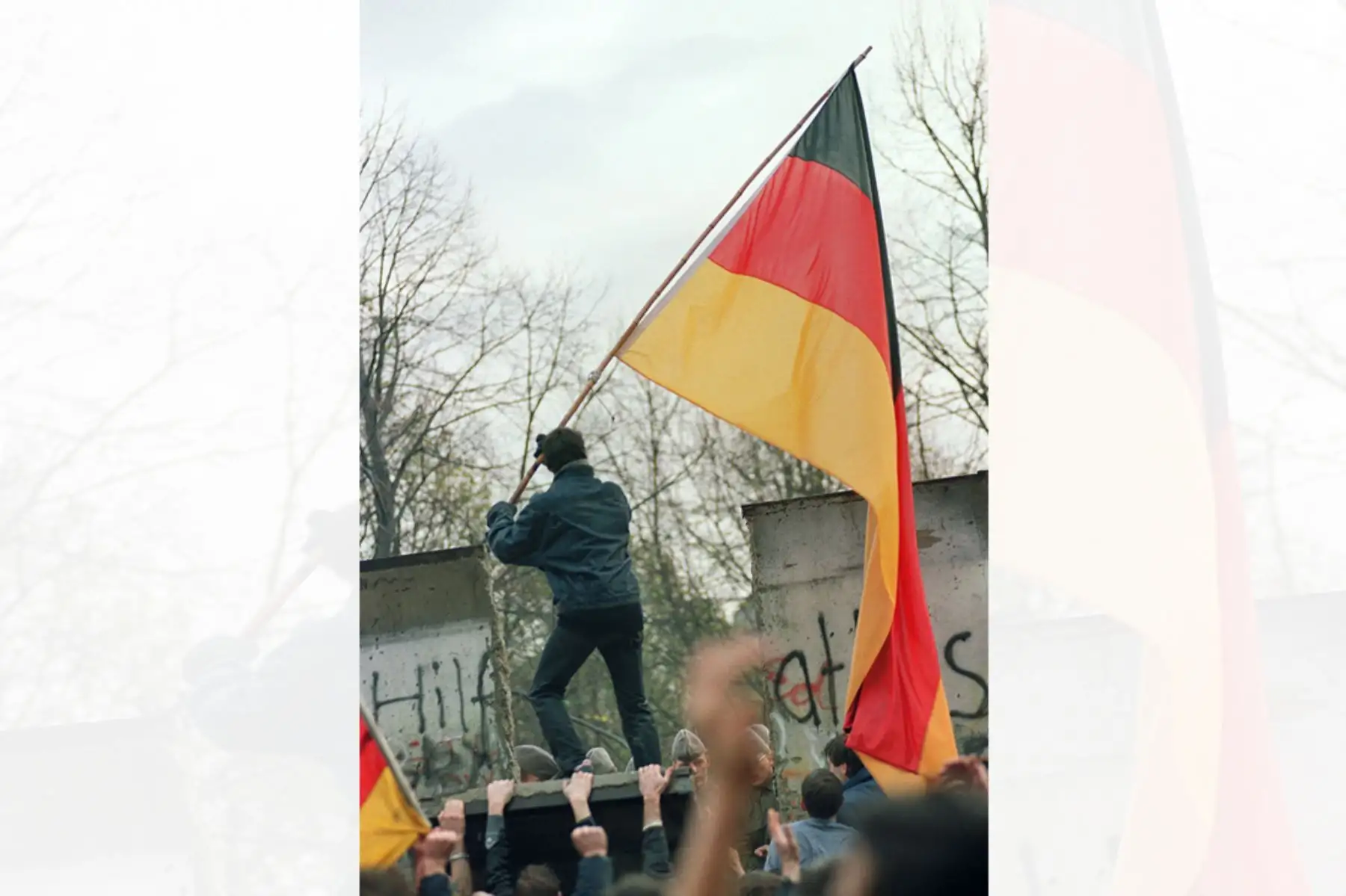 Un berlinés occidental se prepara para entregar una bandera de Alemania a los berlineses orientales a través de una parte del Muro de Berlín caído cerca de la Puerta de Brandenburgo el 11 de noviembre de 1989. Foto: AFP