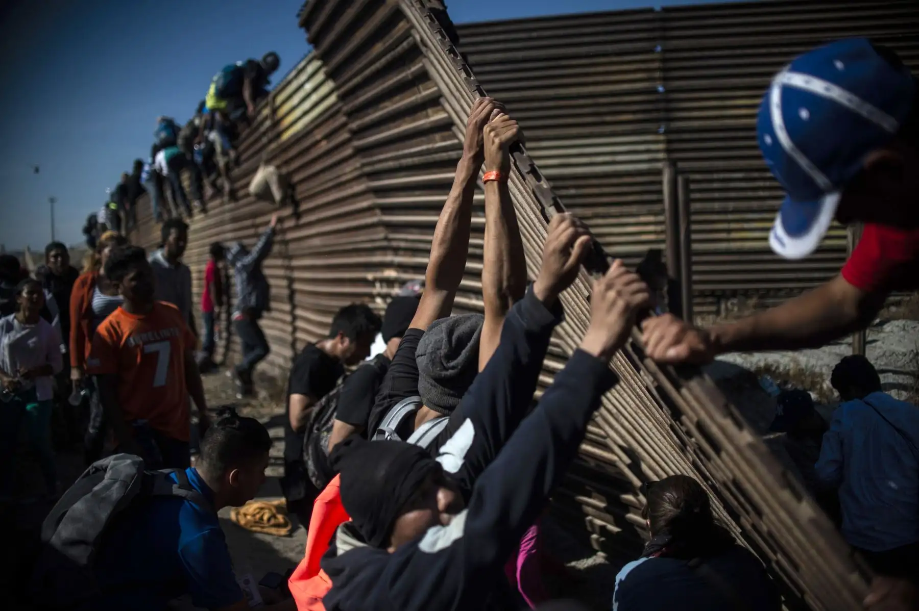 Un grupo de migrantes centroamericanos, principalmente hondureños, trepan la frontera entre México y Estados Unidos mientras otros intentan derribarla, cerca del cruce fronterizo de El Chaparral, en Tijuana, estado de Baja California, México. Cientos de migrantes intentaron asaltar una cerca fronteriza que separa a México de los EE. UU. El domingo, en medio de temores de que se quedarán en México mientras se procesan sus solicitudes de asilo. Un fotógrafo de la AFP dijo que los migrantes se separaron de una