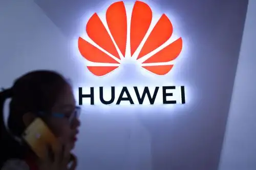 Una mujer usa su teléfono móvil frente a un logotipo de Huawei en la Exposición Internacional de Electrónica de Consumo de Beijing Foto: AFP