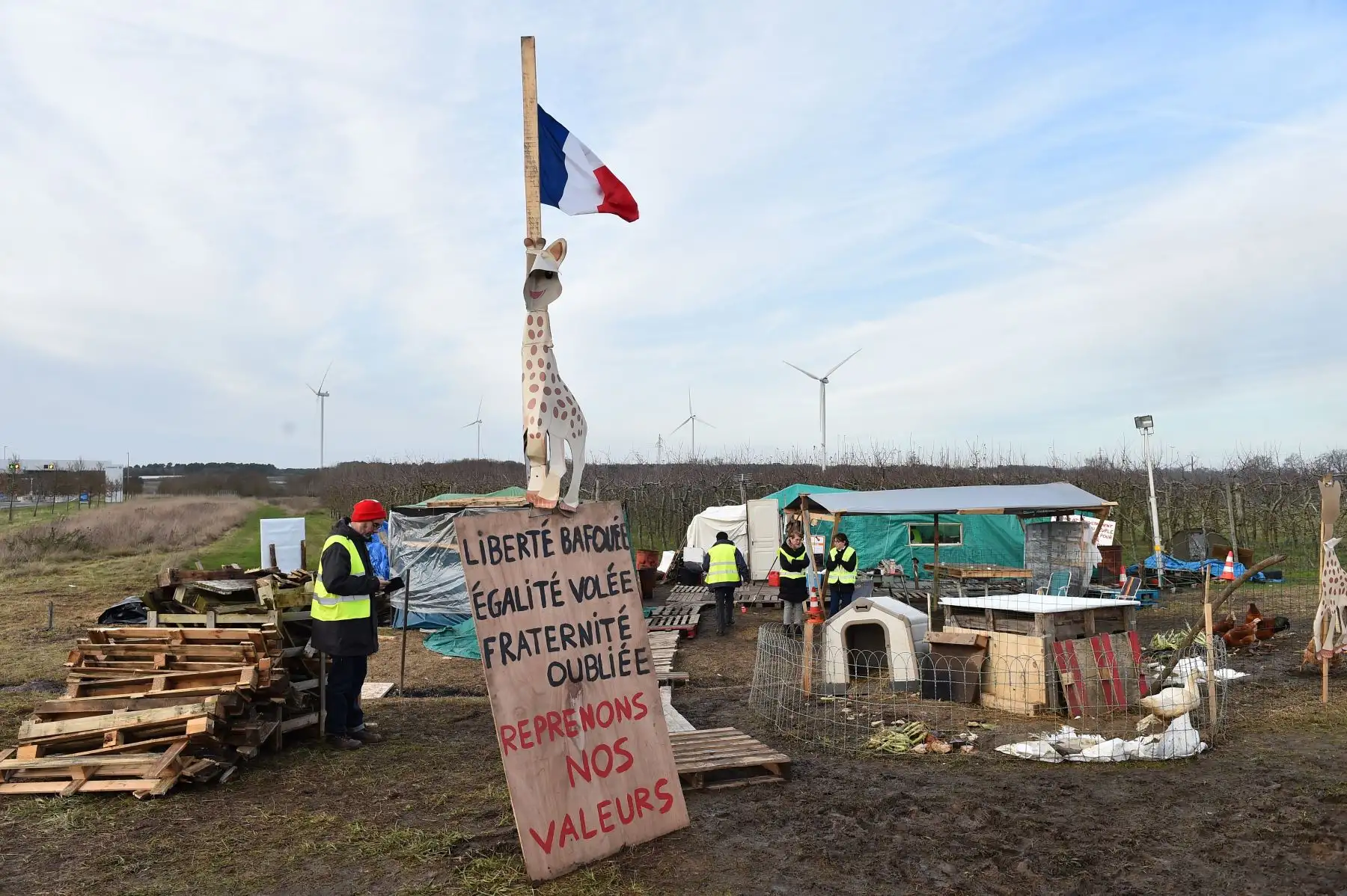 Un manifestante de chaleco amarillo se encuentra junto a un letrero que dice "Libertad despreciado, robo de la igualdad, fraternidad olvidada, recuperemos nuestros valores", y un gallinero al borde de la autopista A28, en Montabon. AFP