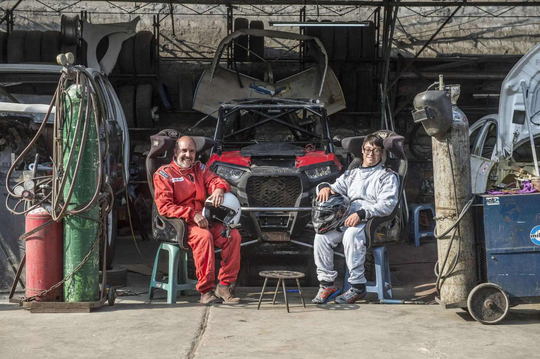 Jacques Barron (R) sonríe al lado de su hijo y copiloto Lucas Barron, de 25 años, en un taller de mecánica donde se está preparando su automóvil para participar en el próximo Rally Dakar. Foto: AFP