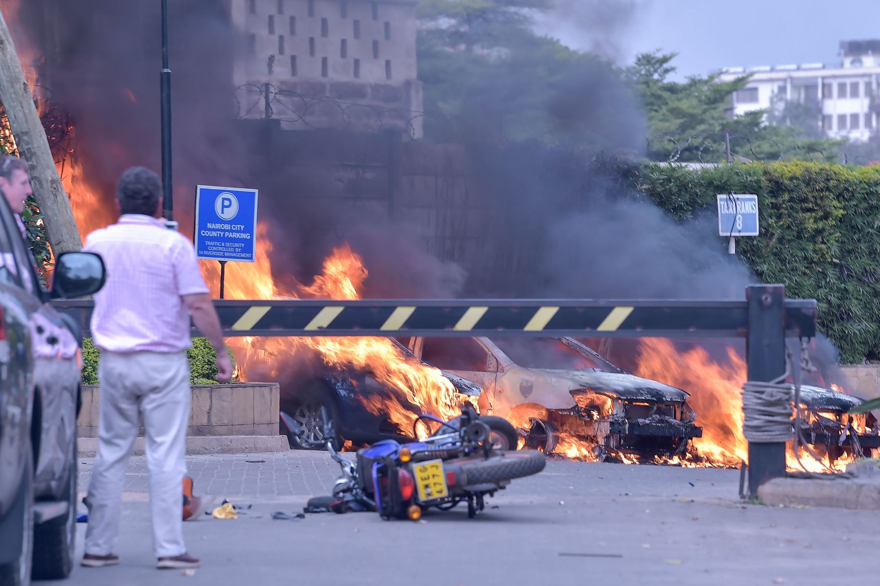 Dos hombres están parados al lado de los autos en llamas en el lugar de una explosión en un complejo hotelero en Nairobi el 15 de enero de 2019 Foto: AFP