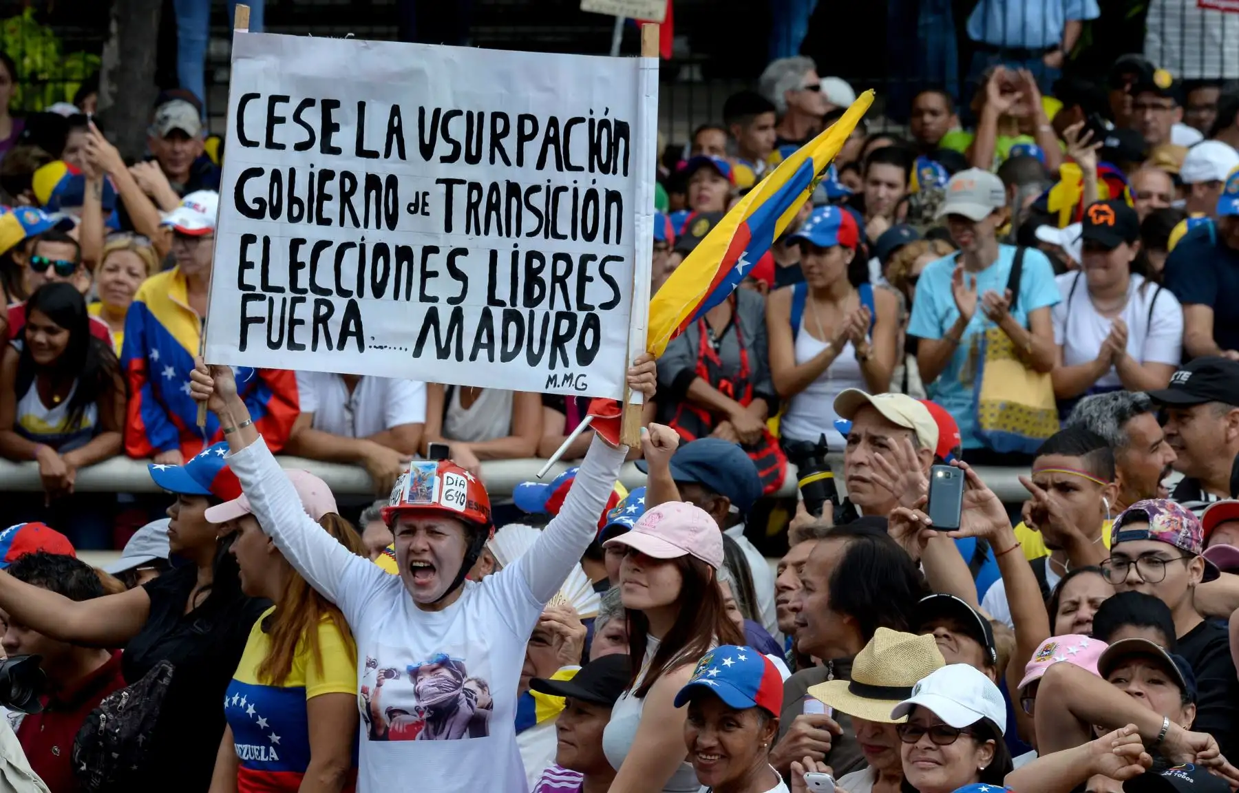 Una mujer sostiene un cartel que exige elecciones libres, entre otras cosas, durante un mitin de oposición en masa contra el líder Nicolas Maduro en el que el jefe de la Asamblea Nacional de Venezuela, Juan Guaido (fuera de trama), se declaró a sí mismo "presidente interino" del país, en el aniversario de un levantamiento de 1958. que derrocó a una dictadura militar en Caracas el 23 de enero de 2019. "Juro asumir formalmente los poderes ejecutivos nacionales como presidente interino de Venezuela. AFP
