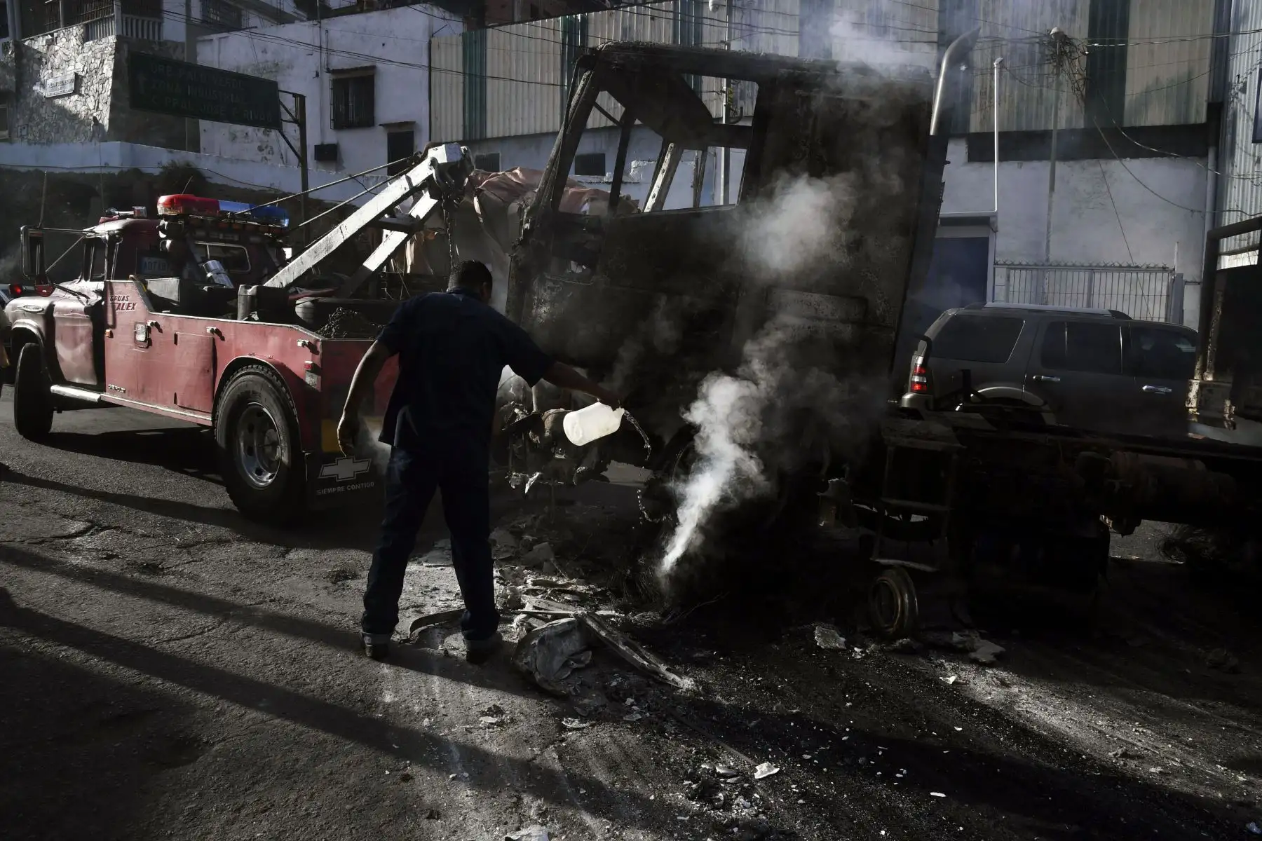 Un hombre intenta apagar el fuego mientras los trabajadores usan una grúa para mover los restos de un camión que se quemó durante las protestas de la noche anterior en el emblemático vecindario de Petare en Caracas, el 24 de enero de 2019. - El jefe de la ONU, Antonio Guterres, el jueves. hizo un llamado al diálogo para detener la crisis política de Venezuela fuera de control, luego de que el líder opositor Juan Guaido se declarara a sí mismo presidente interino.  AFP
