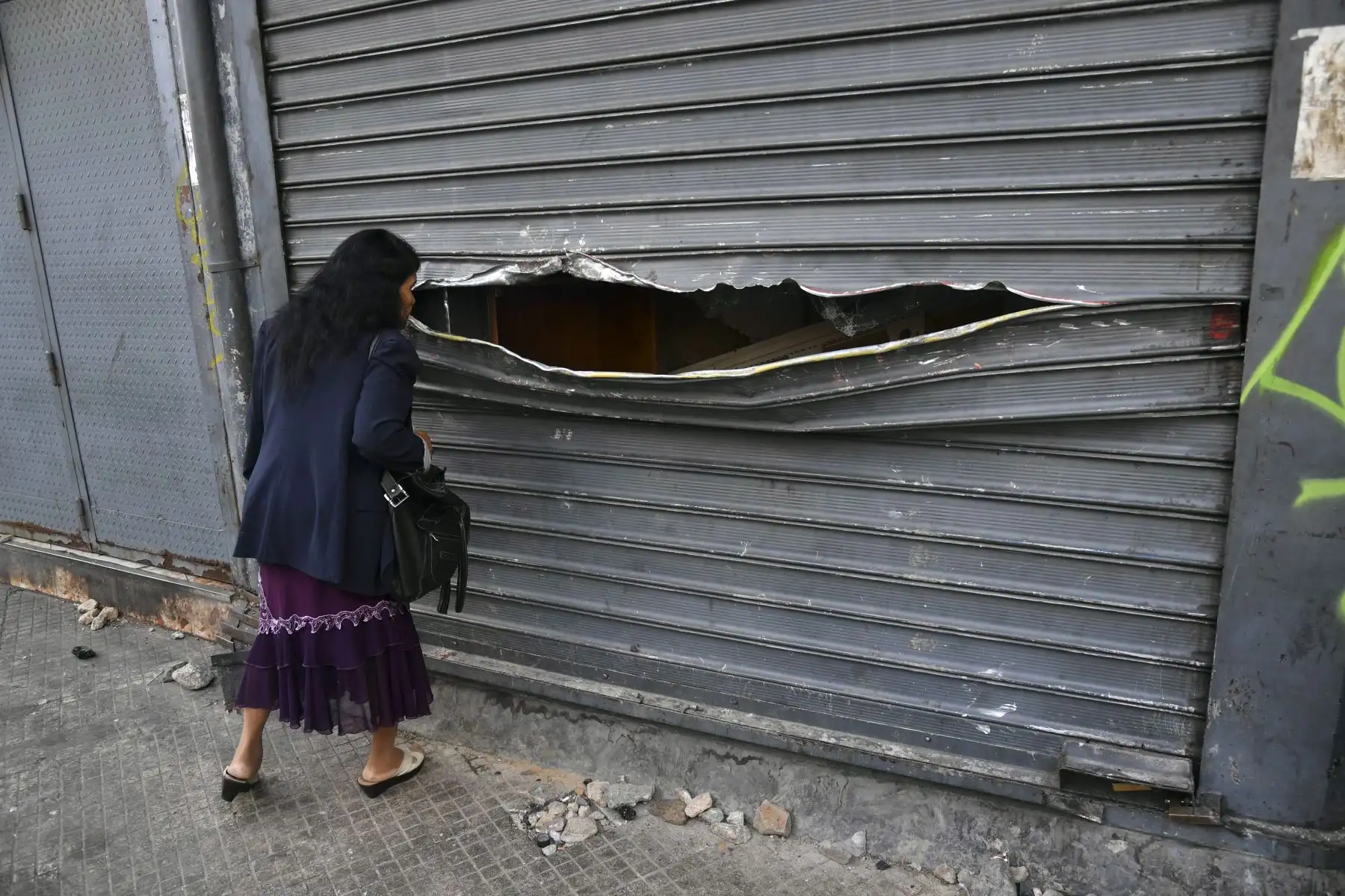 Una mujer mira a través de la vandalizada cortina de una tienda que fue saqueada durante las protestas de la noche anterior en Caracas, Venezuela, el 24 de enero de 2019. - El jefe de la ONU, Antonio Guterres, pidió el jueves un diálogo para detener la crisis política de Venezuela que está fuera de control, después de la oposición. El líder Juan Guaido se declaró presidente interino. AFP