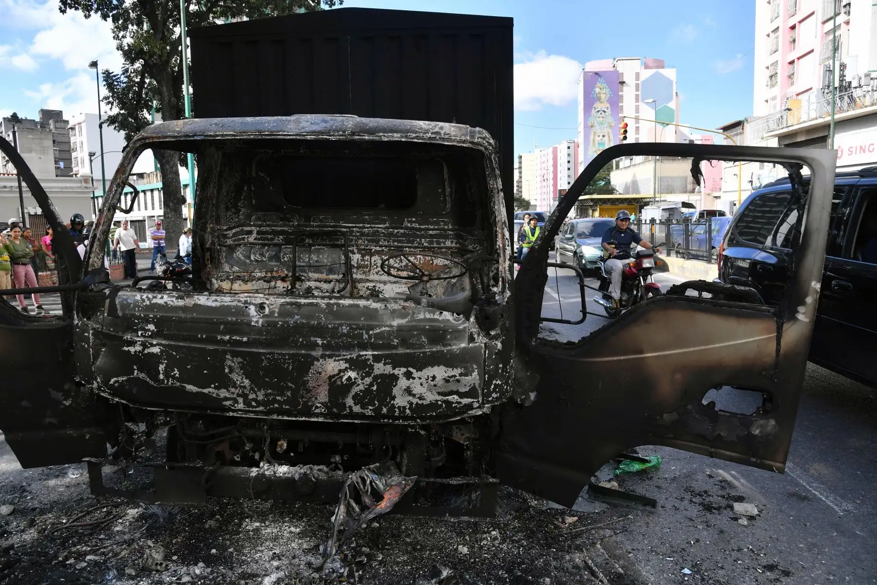 Un motociclista pasa por encima de los restos de un camión del gobierno que se quemó durante las protestas la noche anterior en Caracas, el 24 de enero de 2019. - El jefe de la ONU, Antonio Guterres, pidió el jueves un diálogo para detener la crisis política de Venezuela que está fuera de control, después de la oposición. El líder Juan Guaido se declaró presidente interino.  AFP