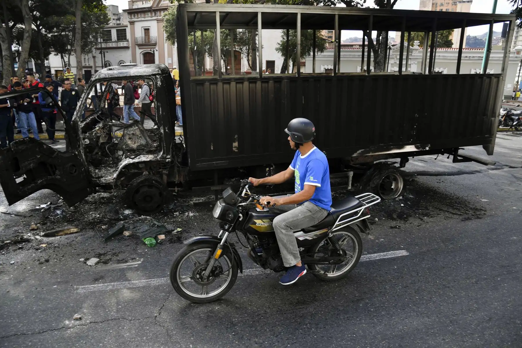 Un motociclista pasa por encima de los restos de un camión del gobierno que se quemó durante las protestas la noche anterior en Caracas, el 24 de enero de 2019. - El jefe de la ONU, Antonio Guterres, pidió el jueves un diálogo para detener la crisis política de Venezuela que está fuera de control, después de la oposición. El líder Juan Guaido se declaró presidente interino.  AFP