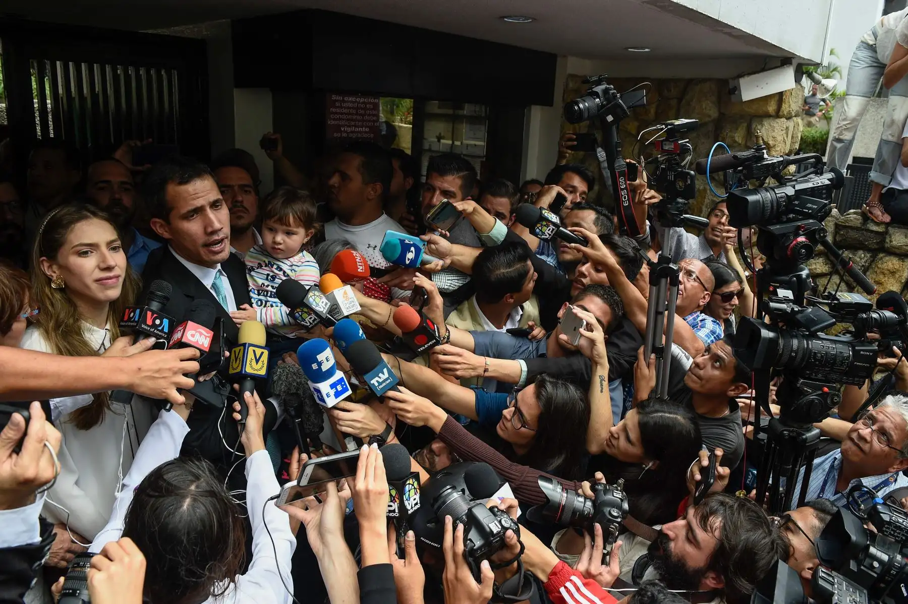 El líder de la oposición y autoproclamado "presidente interino" Juan Guaido habla con la prensa mientras sostiene a su hija Miranda, junto a su esposa, Fabiana Rosales. Foto: AFP.