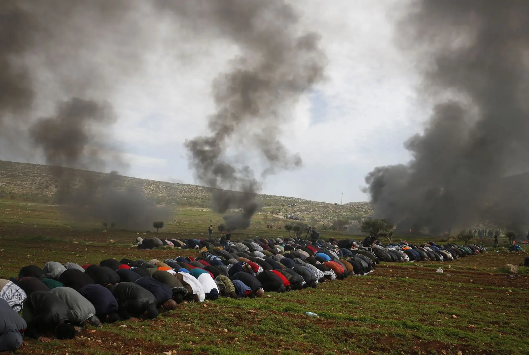 Los palestinos realizan las oraciones del viernes mientras el humo se levanta al quemar neumáticos durante una protesta contra los asentamientos judíos, en la aldea de al-Mughayyir cerca de Ramallah, en la Cisjordania ocupada por Israel. Foto: AFP