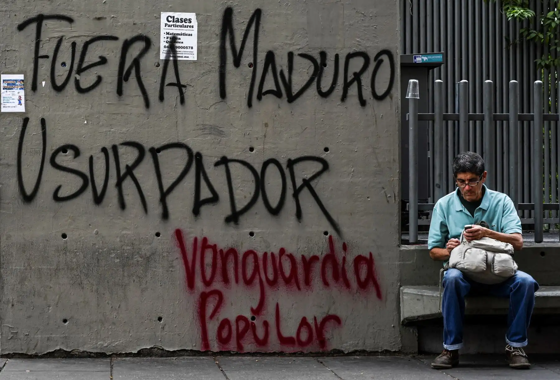 Un hombre se sienta al lado de un graffiti que lee "usurpador de Maduro" en Caracas. AFP
