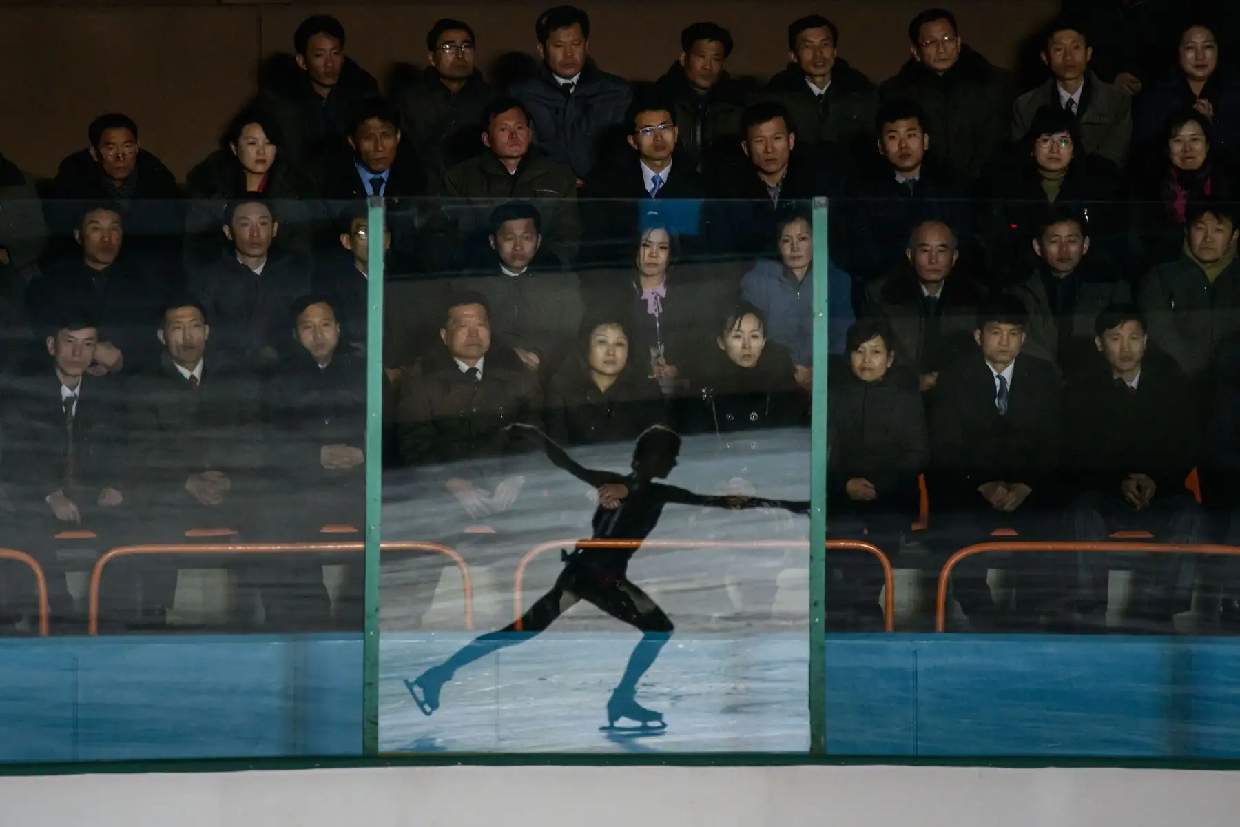 Un patinador sobre hielo se refleja en un panel de vidrio mientras los espectadores asisten al 