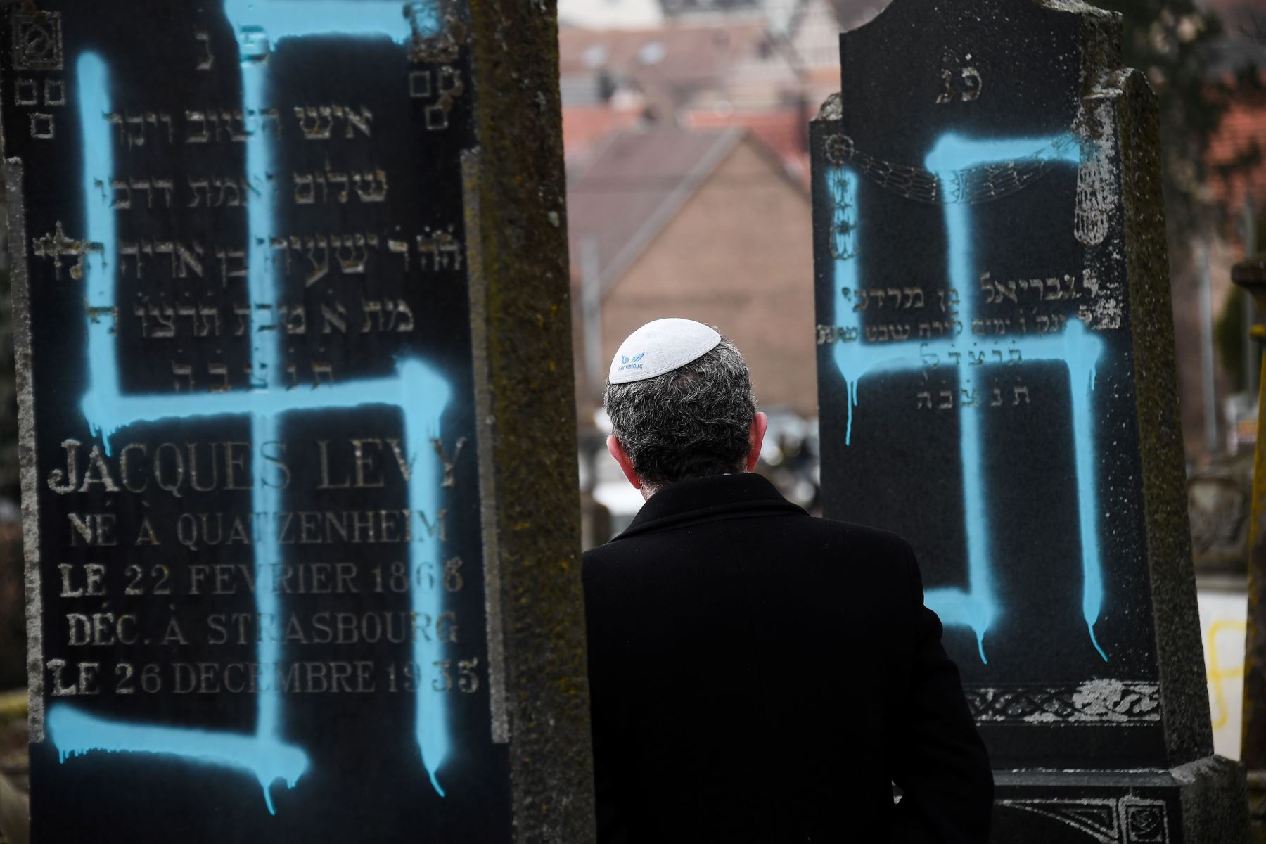 Un hombre camina junto a tumbas destrozadas con esvásticas en el cementerio judío de Quatzenheim, el 19 de febrero de 2019. Foto: AFP