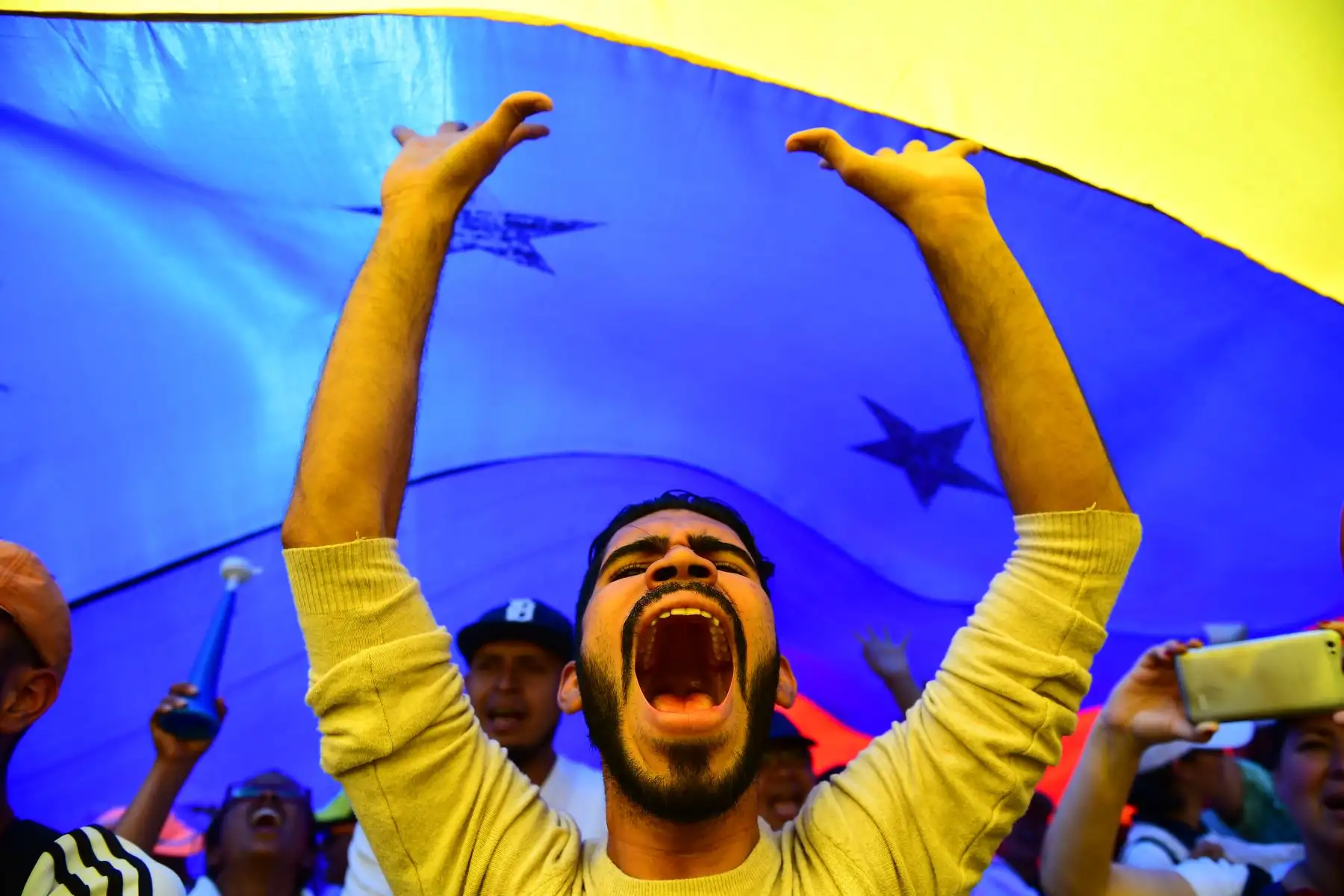 Los partidarios del líder opositor venezolano Juan Guaido están bajo una bandera gigante venezolana durante una protesta en Caracas. AFP