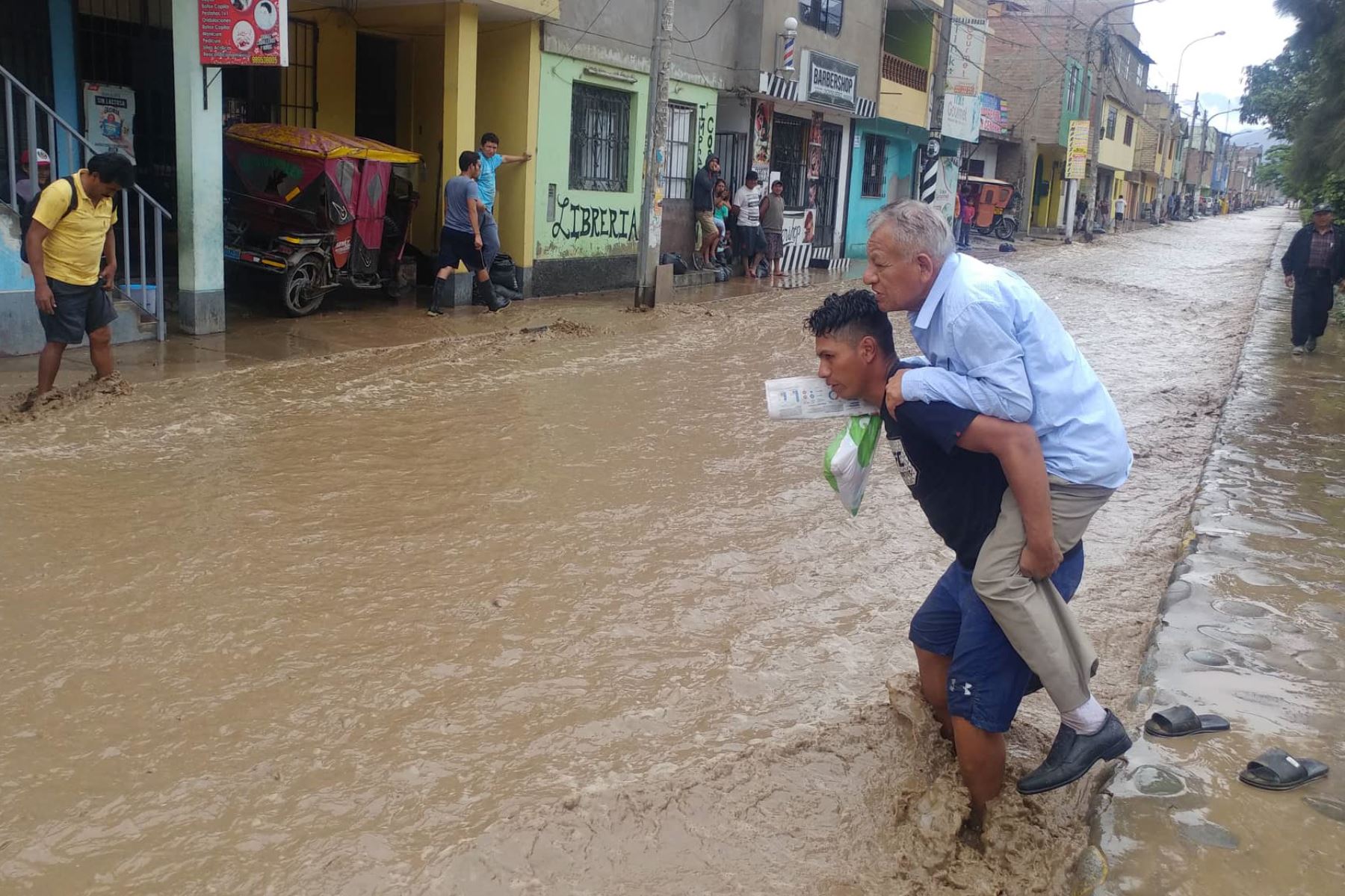 Un vecino joven ayuda a un adulto mayor a cruzar la pista inundada. Foto: Héctor Vinces