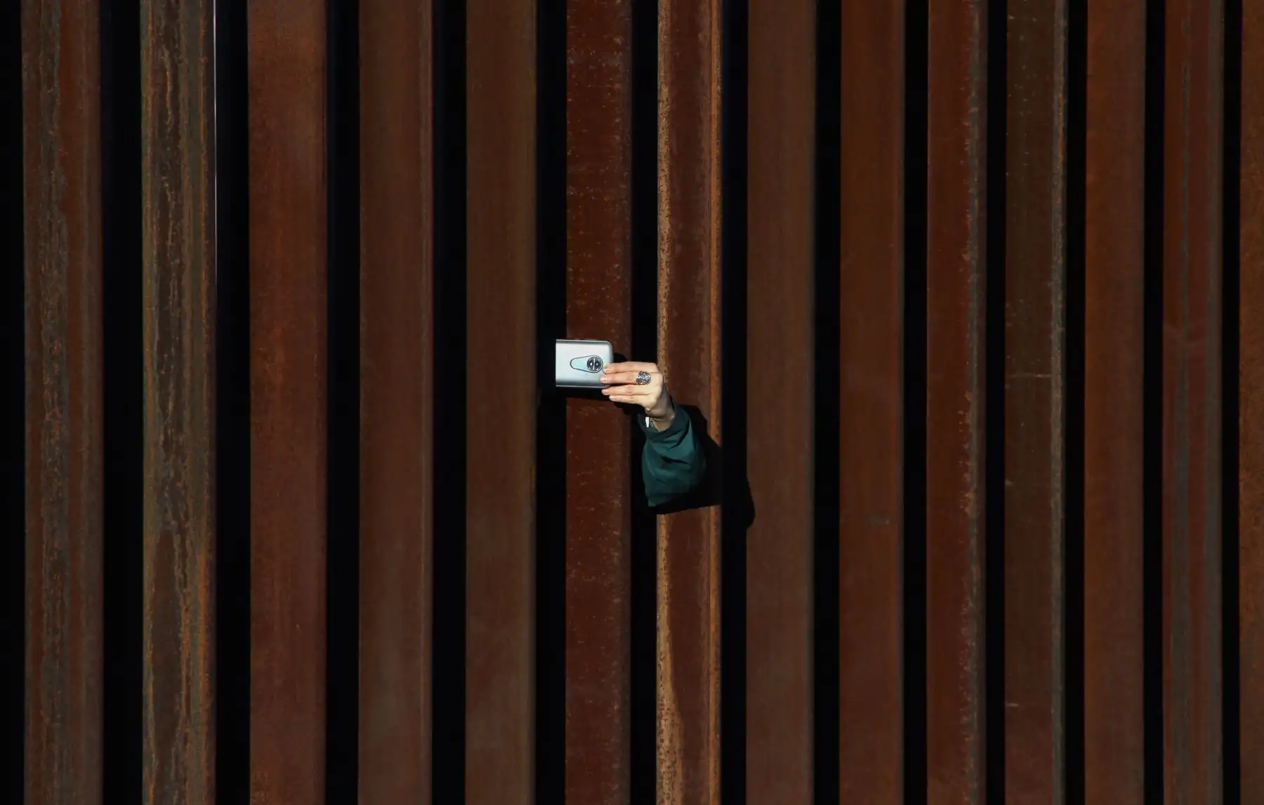 Una mujer en los Estados Unidos toma una foto a México a través de la cerca fronteriza. AFP